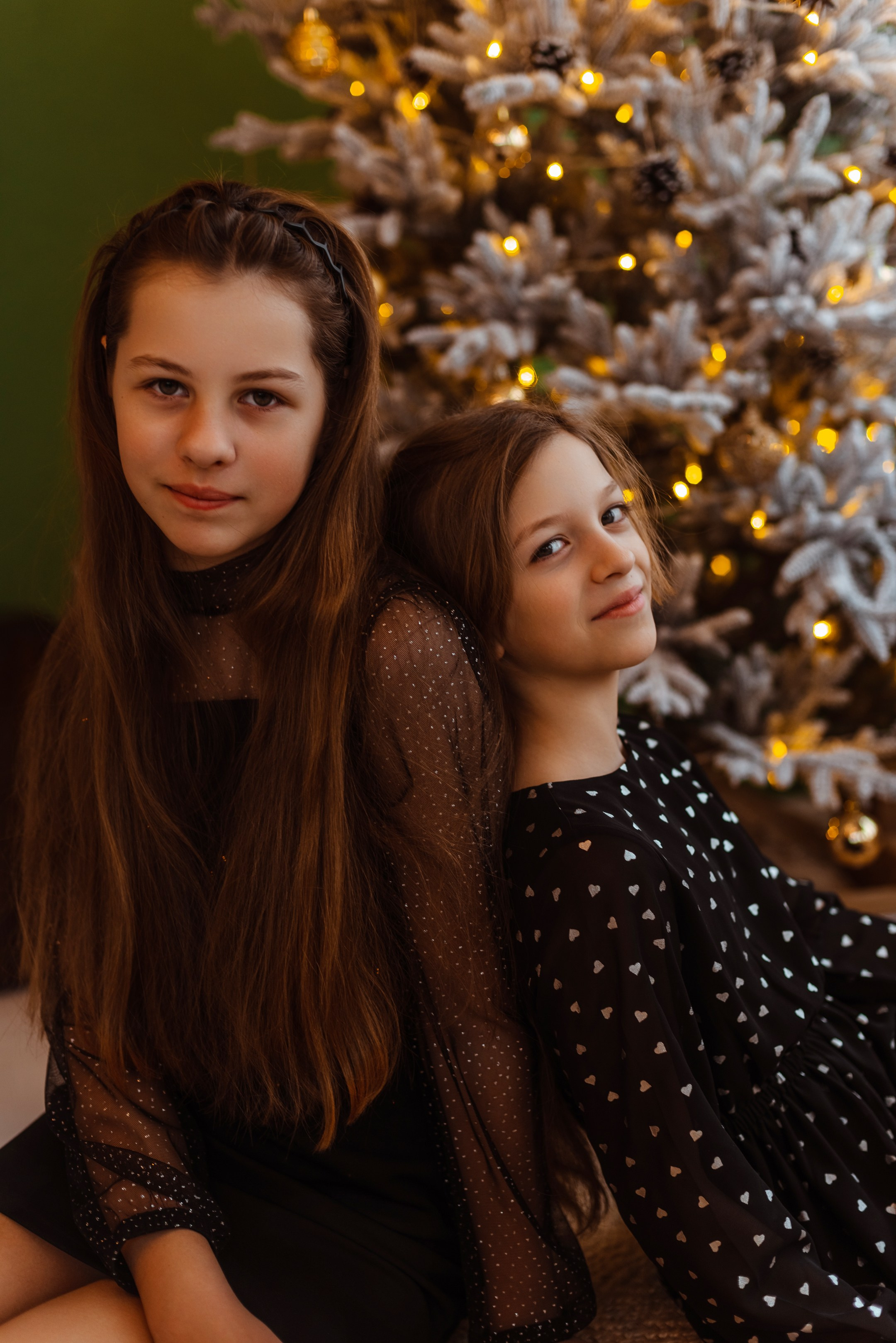 Фотомомент нежности: младшая девочка прижимается к старшей, обе девушки погружены в зимние развлечения и игры