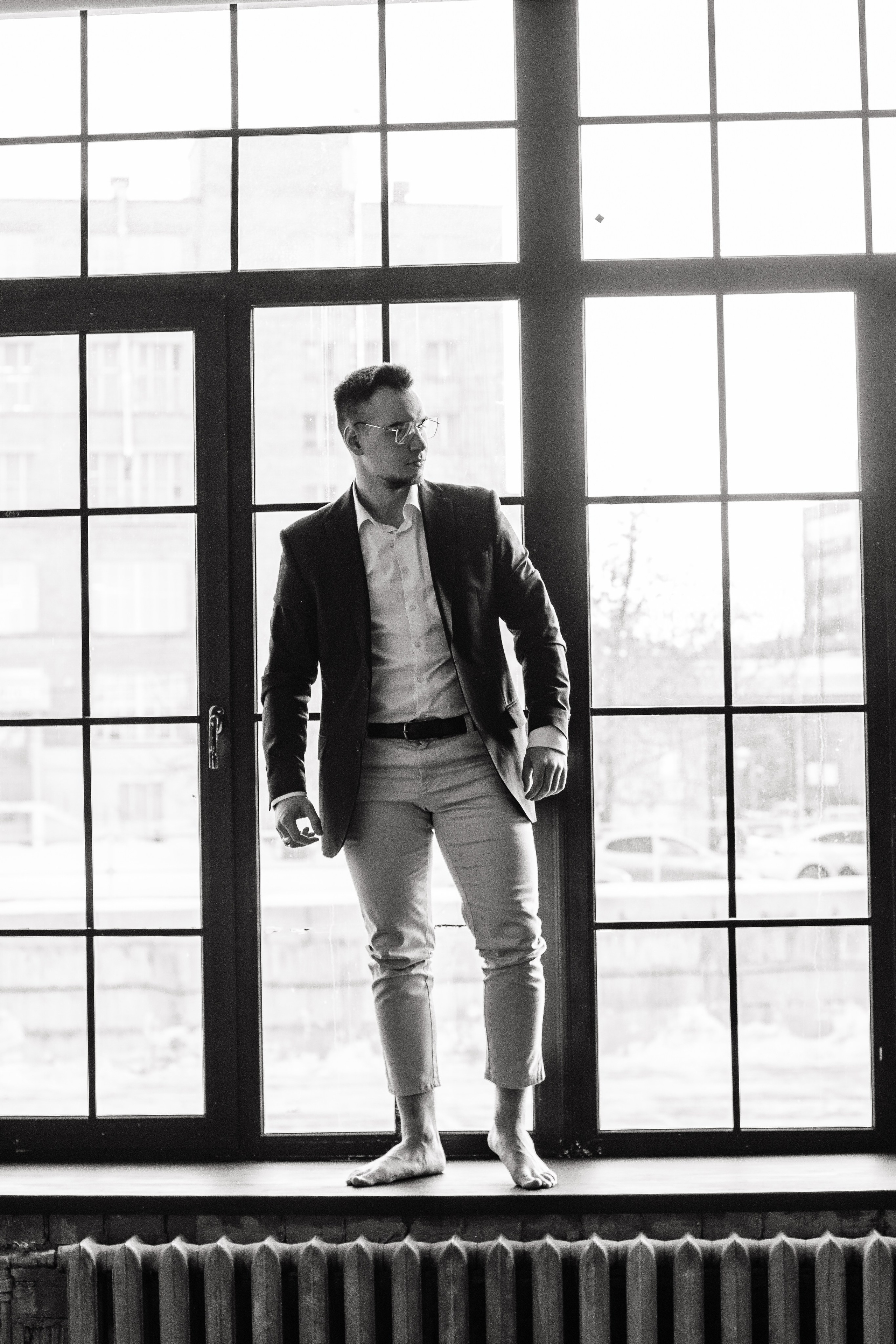 Черно-белый мужской портрет в полный рост на фоне окна.