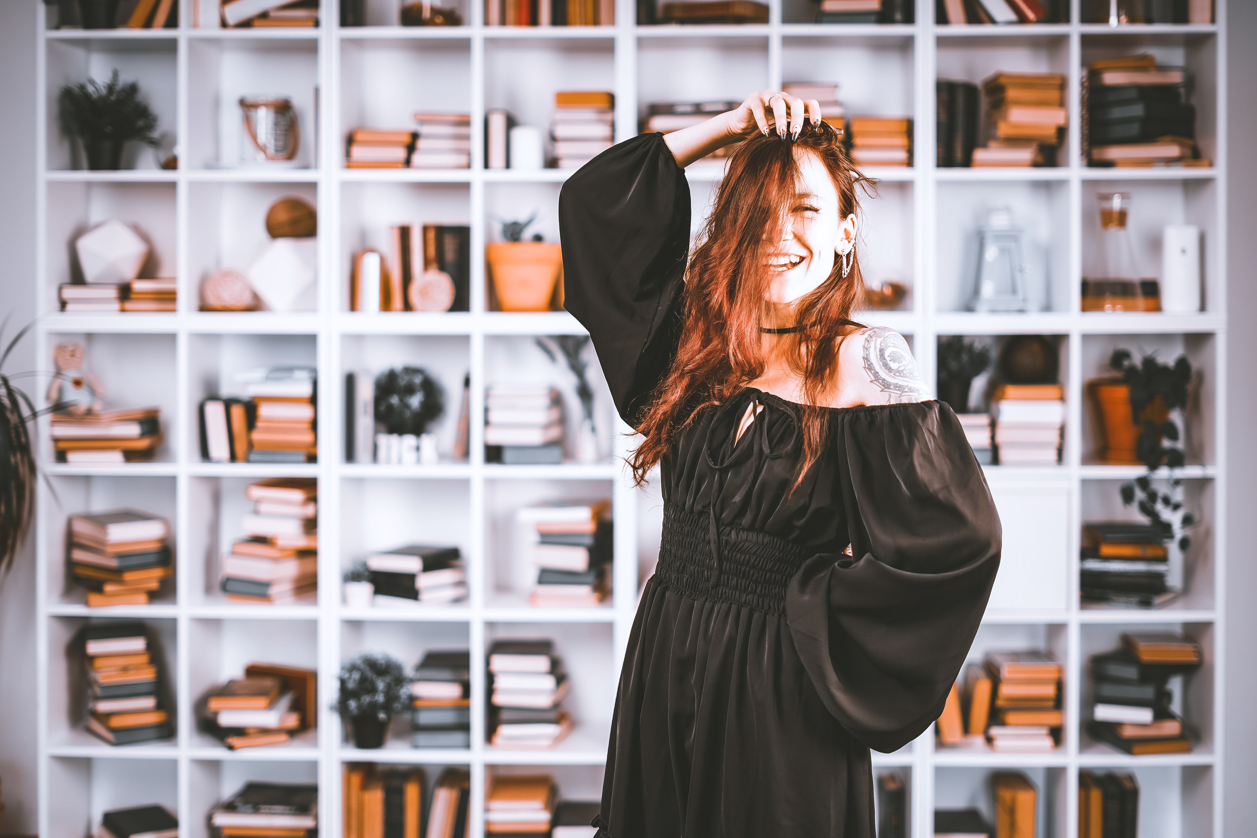 Девушка в красивом черном платье стоит у полки с книгами и смеется