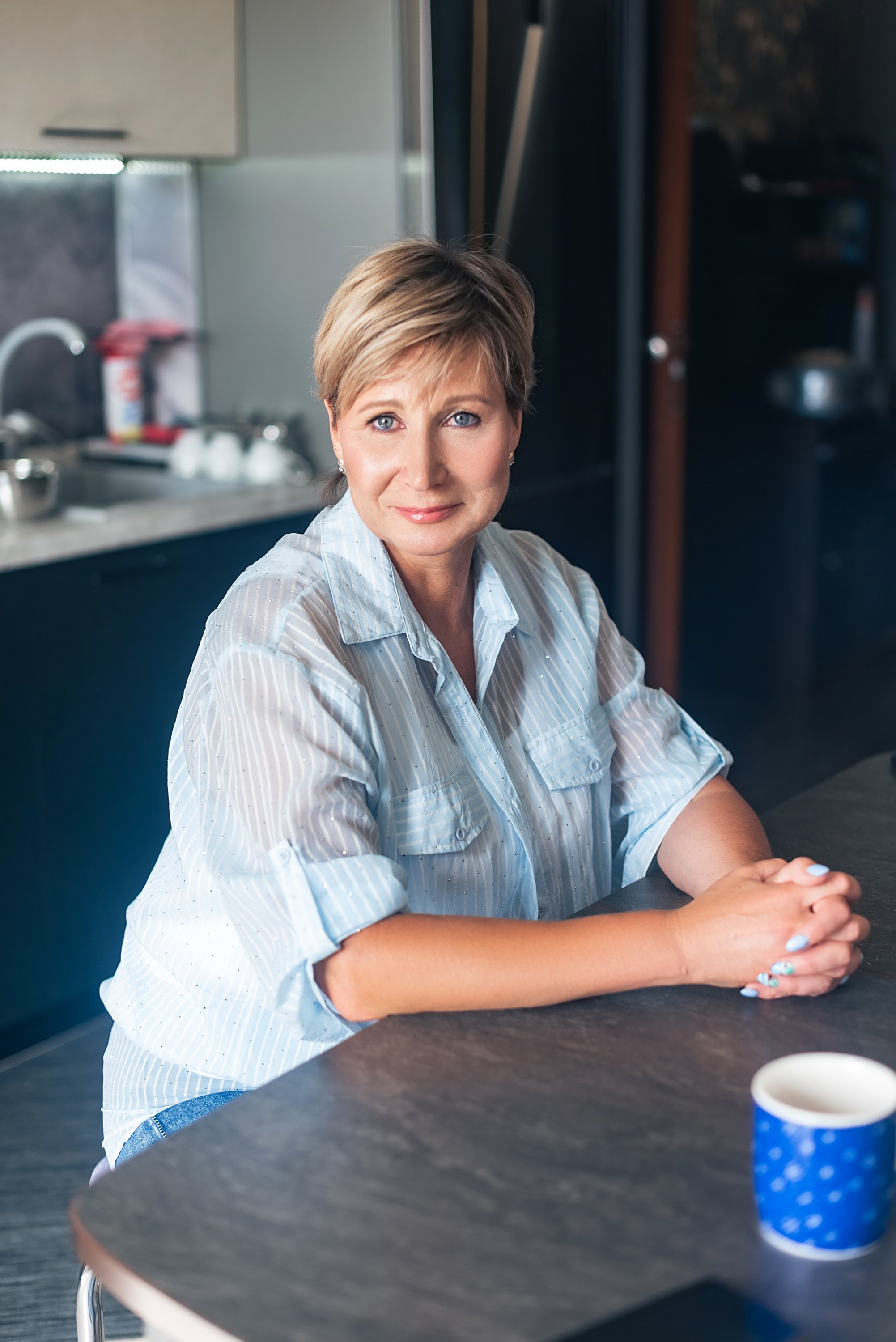 Портрет женщины в голубой рубашке сидит за столом с синей чашкой.