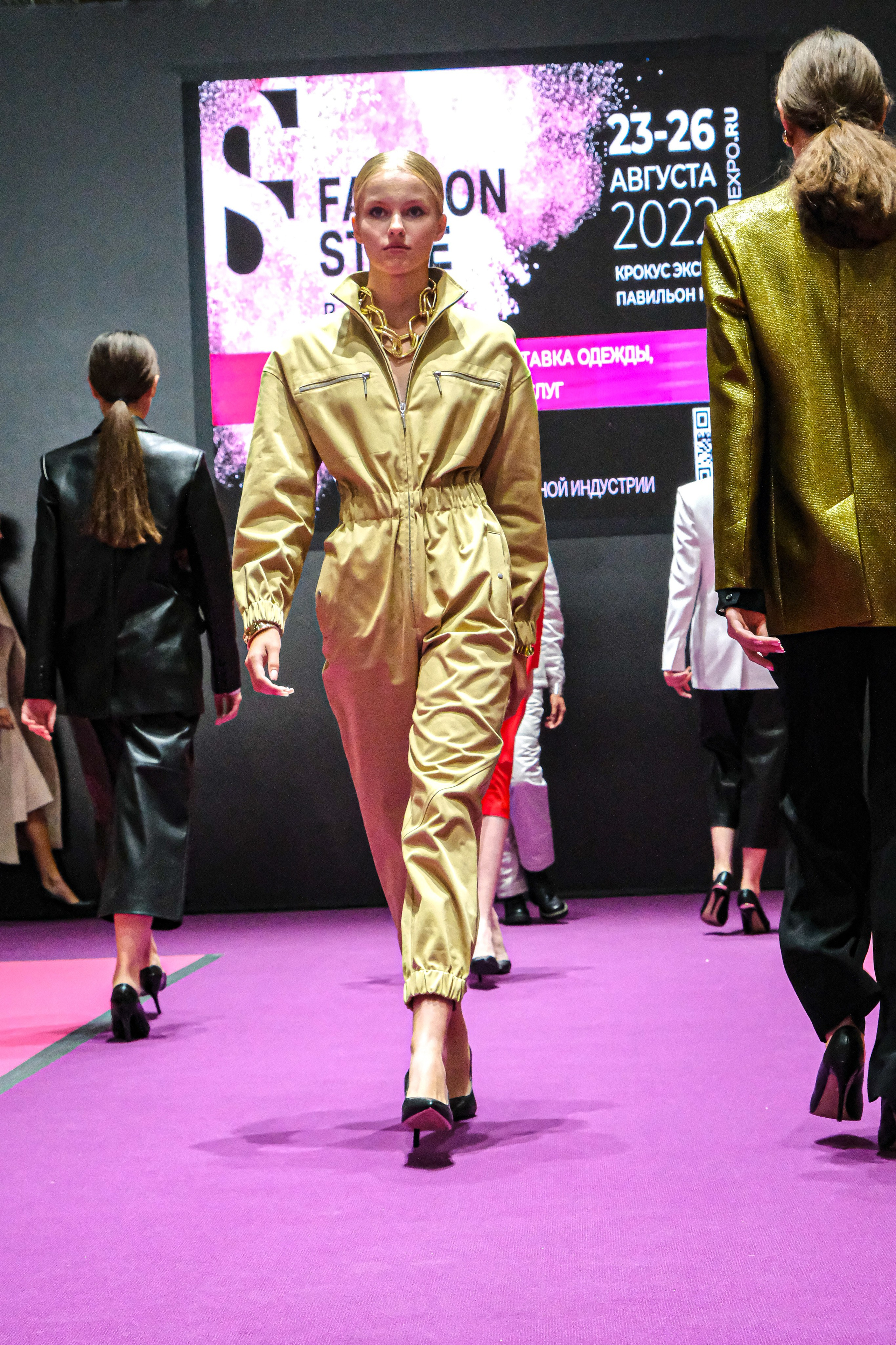  "Модели в ярких нарядах проходят по подиуму во время показа мод, освещенные яркими софитами и окруженные восторженными зрителями."