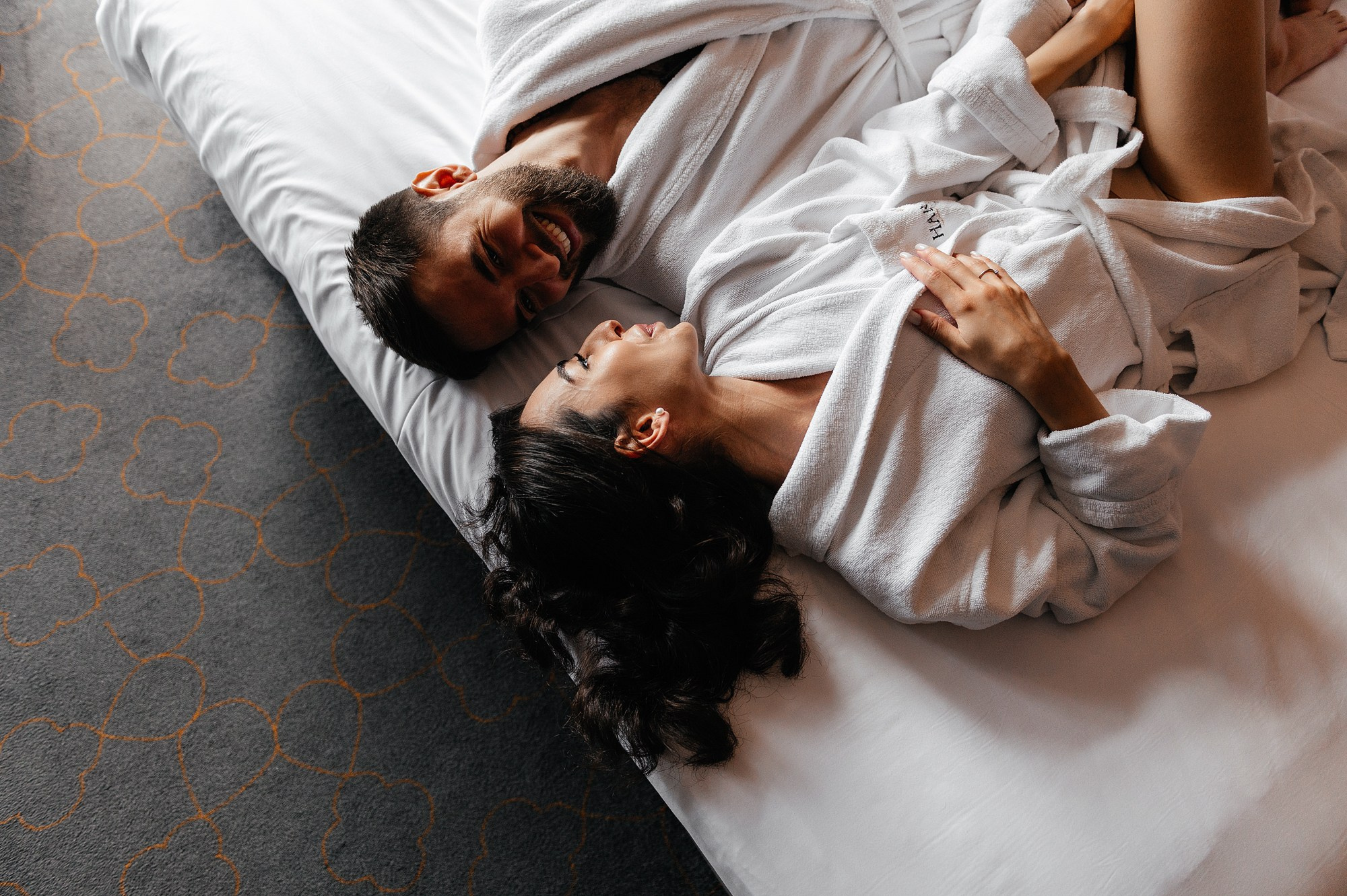 Жених с невестой лежат в халатах на кровати в отеле в москве.