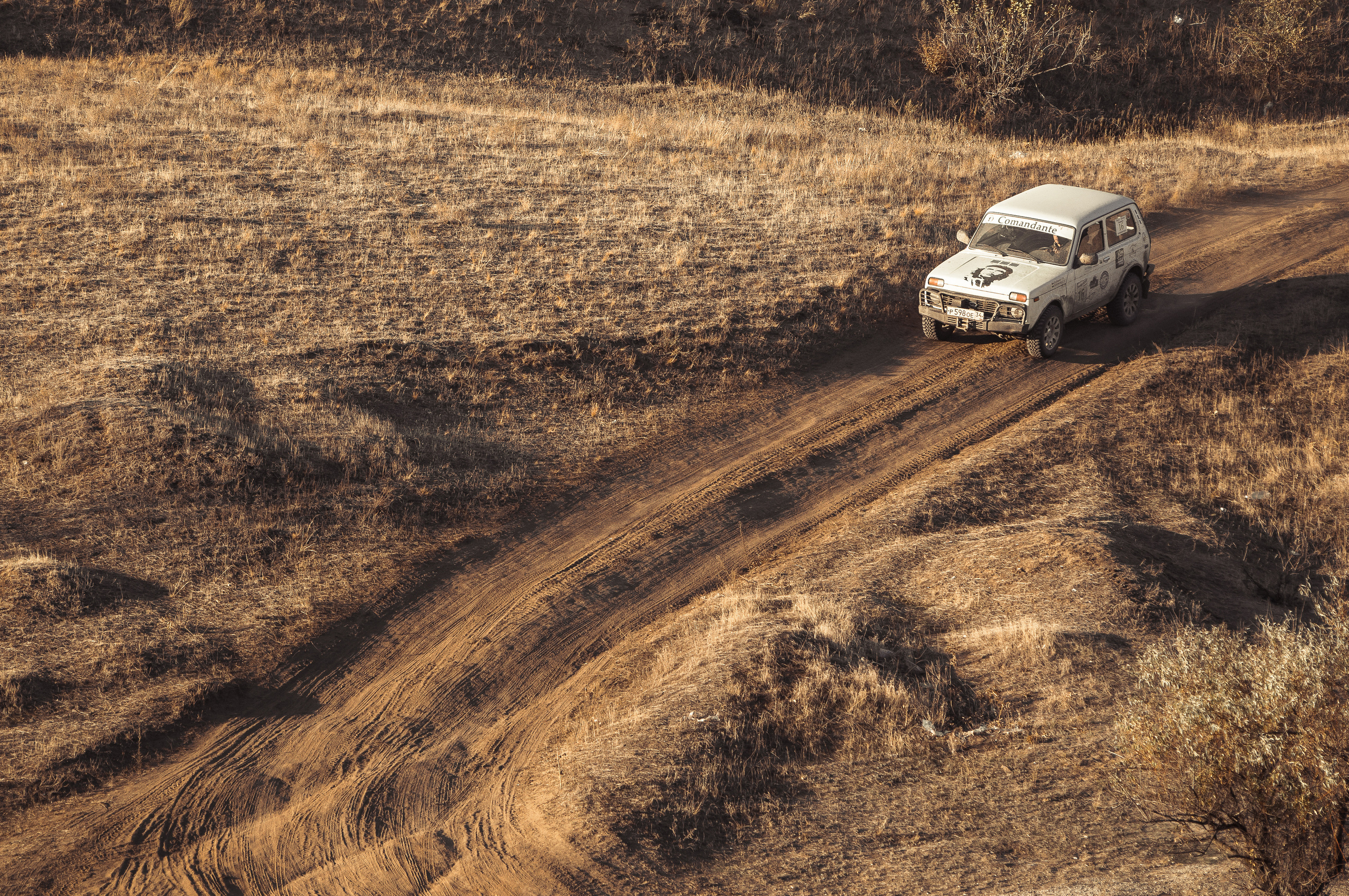 Белый автомобиль Нива едет по грунтовой дороге среди поля