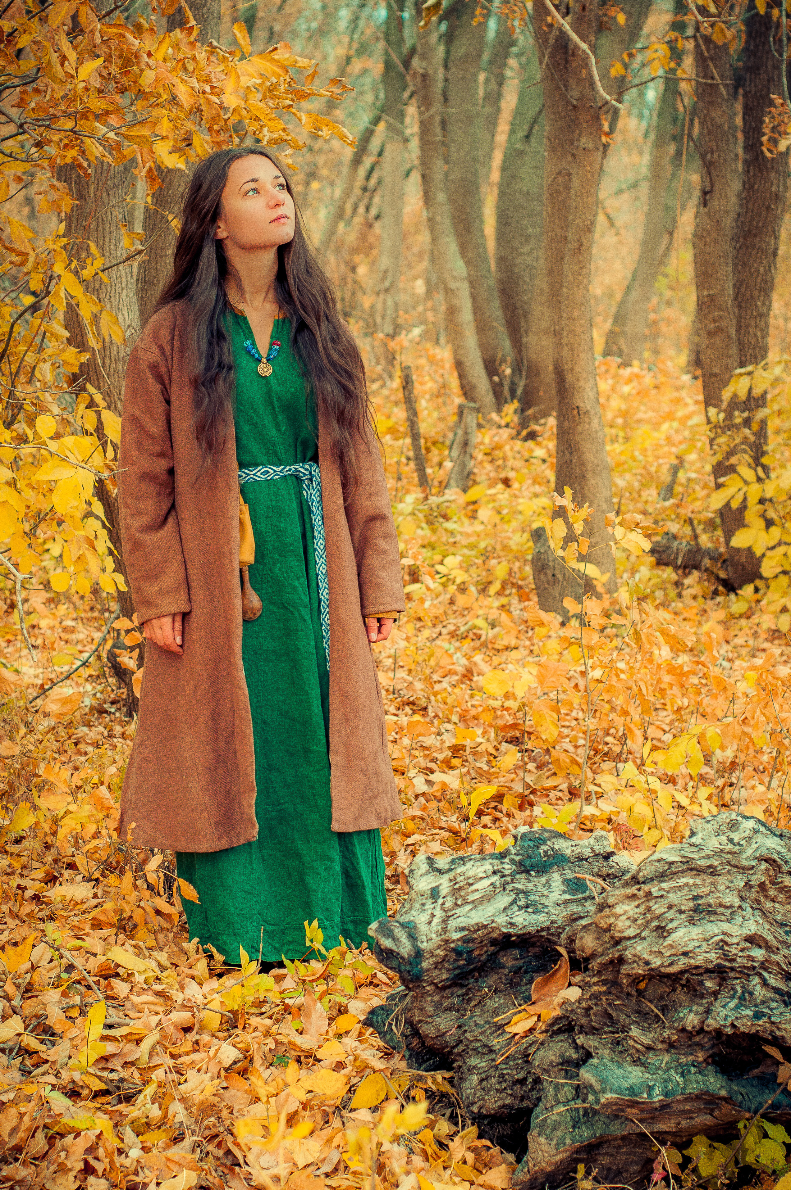 Девушка в зелёном платье стоит в осеннем лесу около камня