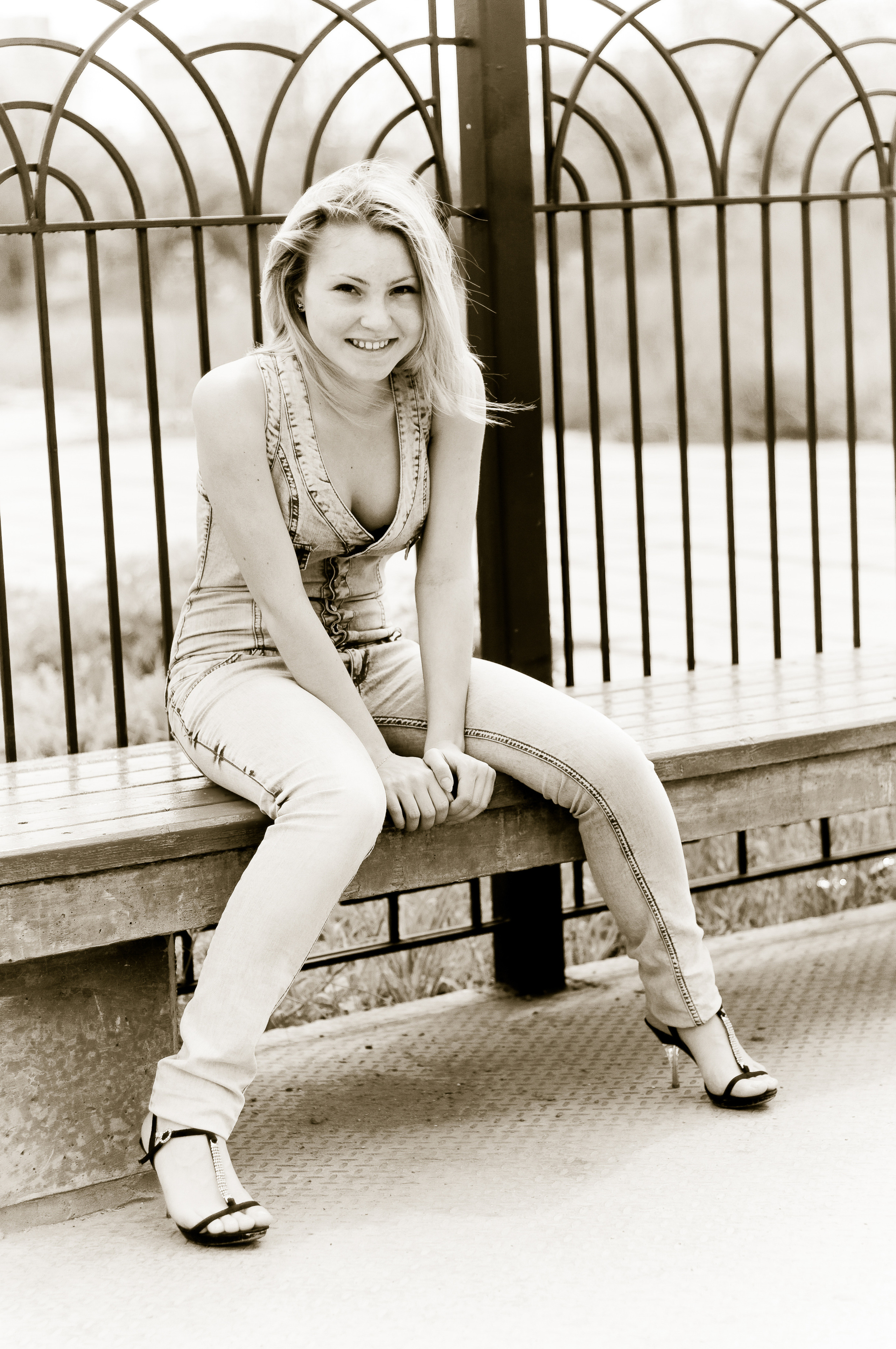 Девушка в джинсовом комбинезоне сидит на скамейке