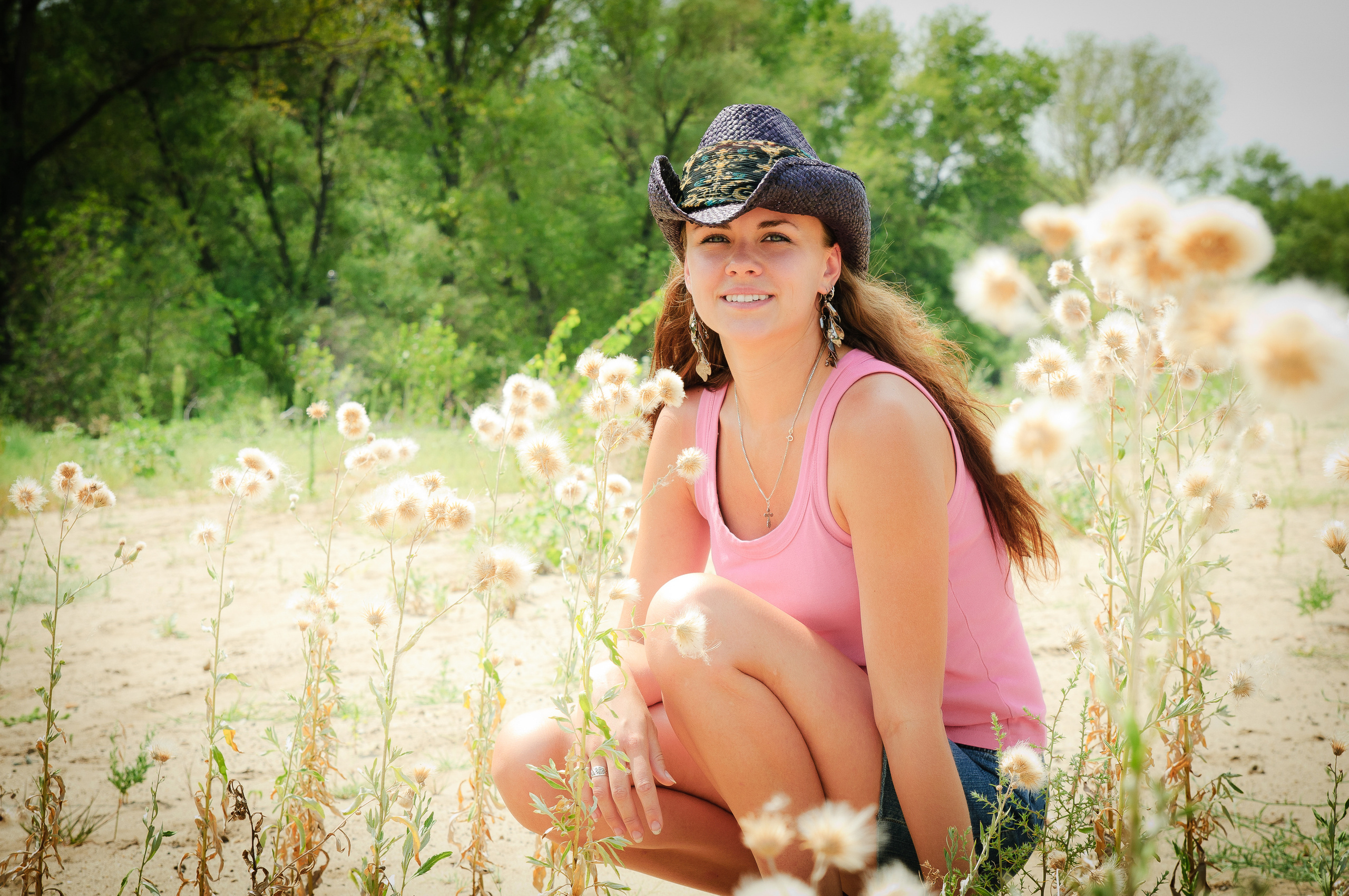 Девушка в розовой майке и ковбойской шляпе сидит в поле