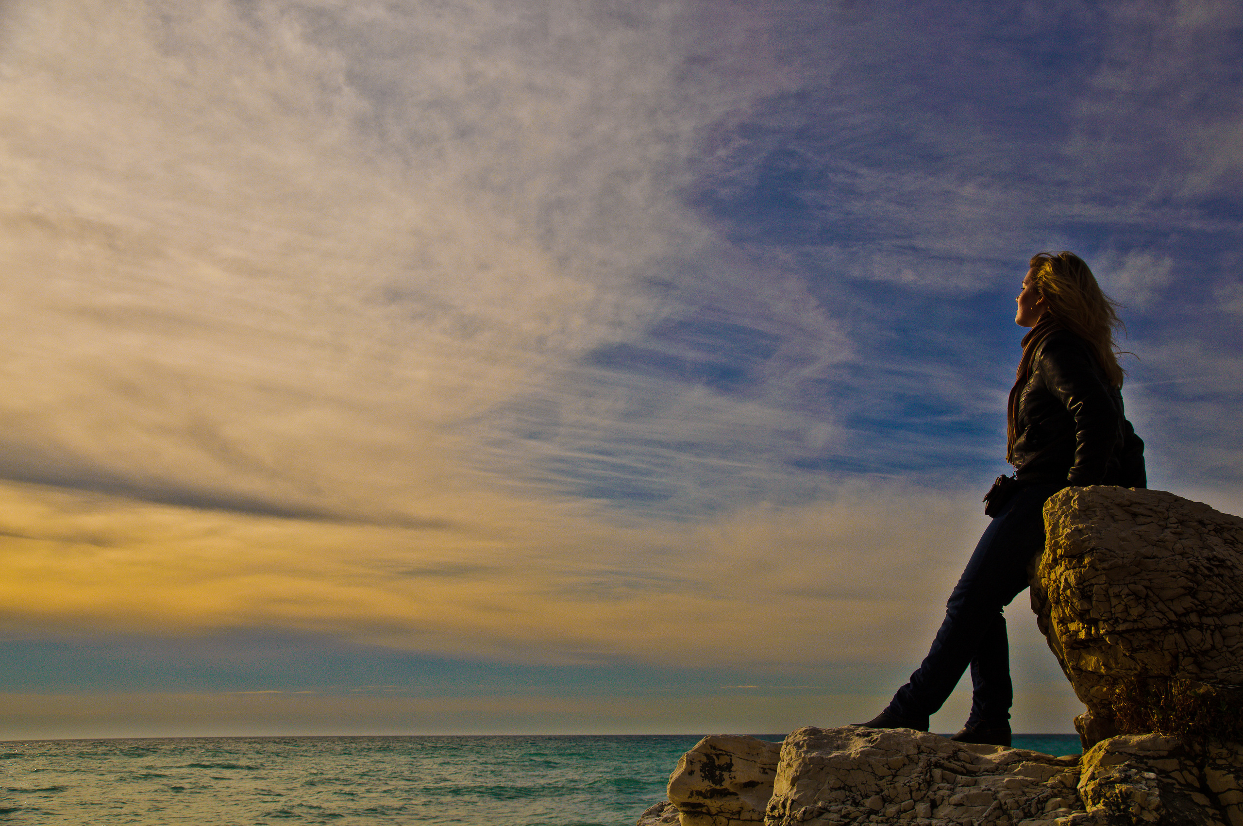 Девушка стоит на скале на побережье море на закате