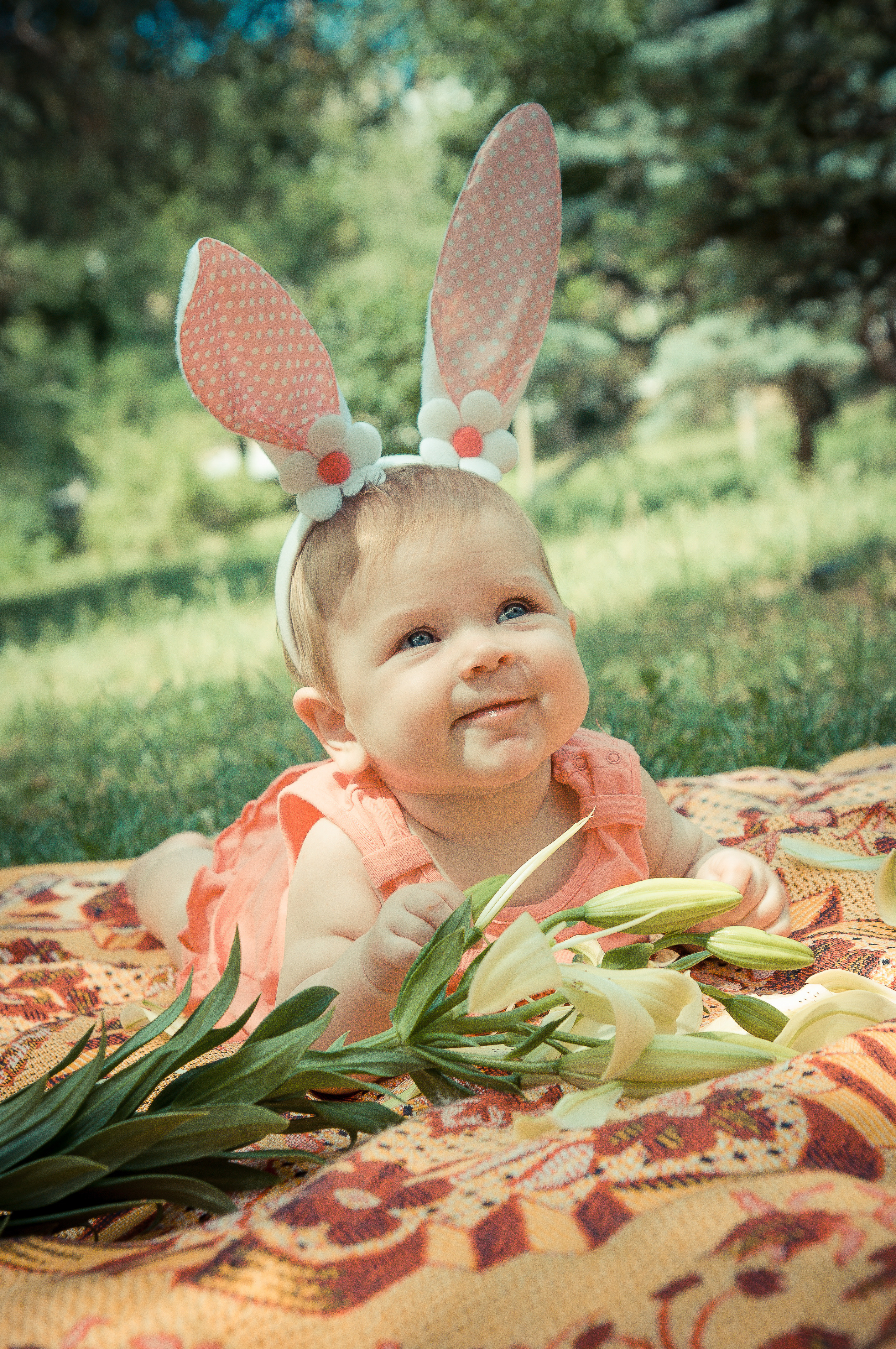 Ребёнок с заячьими ушами лежит на земле среди лилий