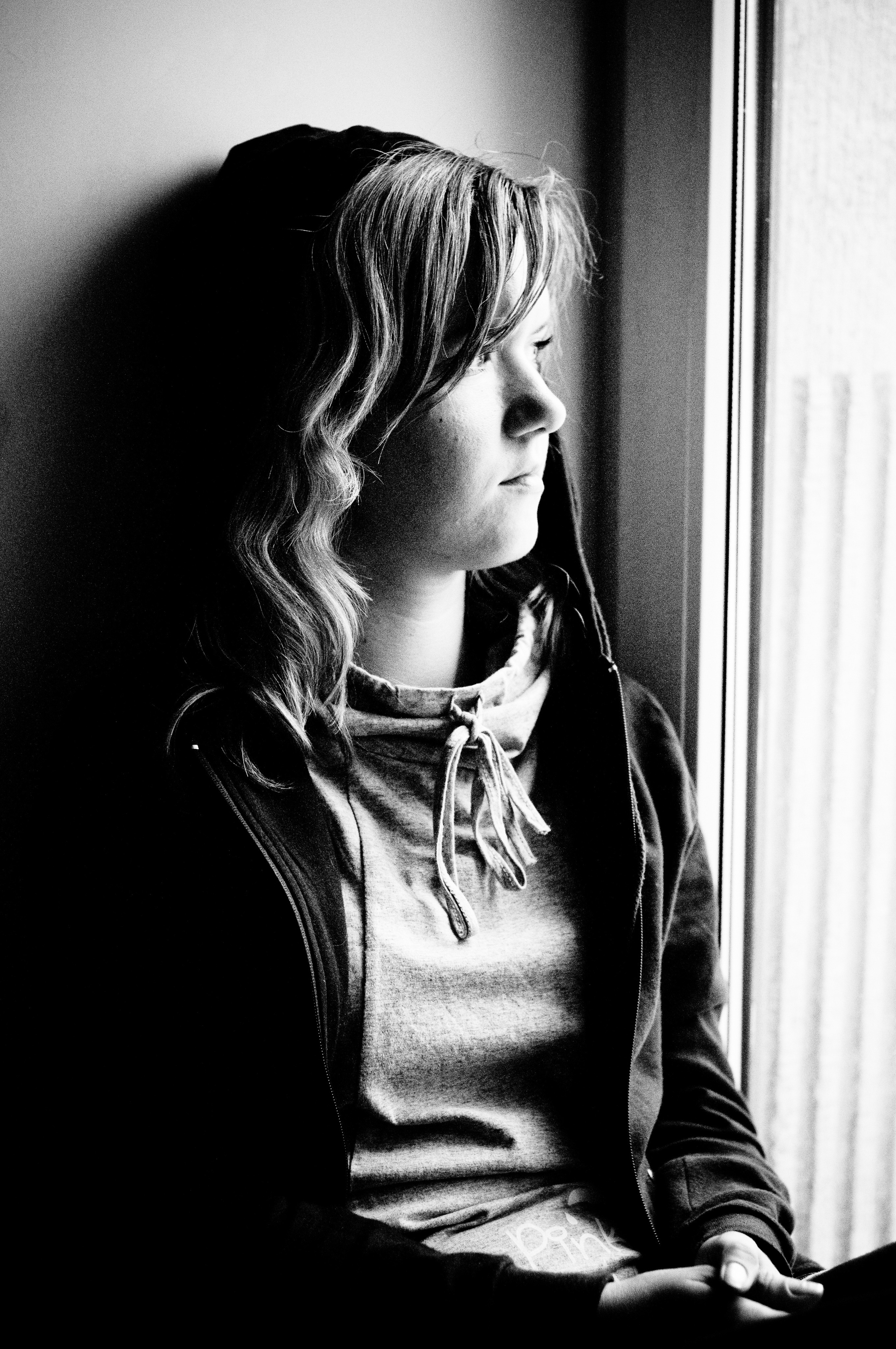 Девушка в капюшоне сидит у окна