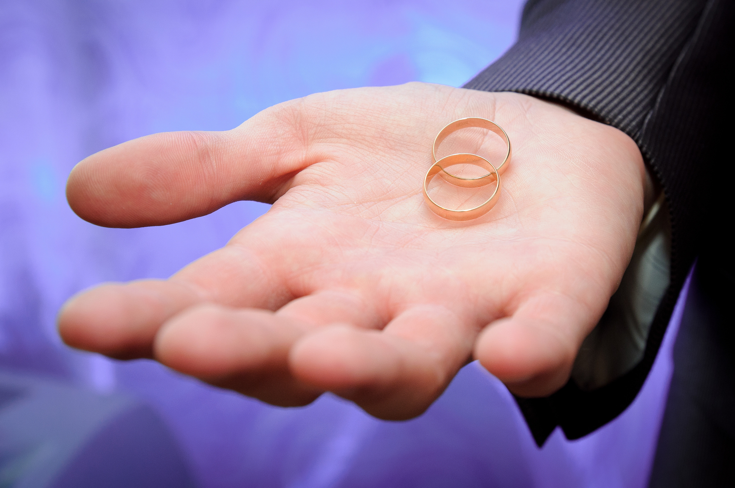 Обручальные кольца лежат на ладони на фиолетовом фоне