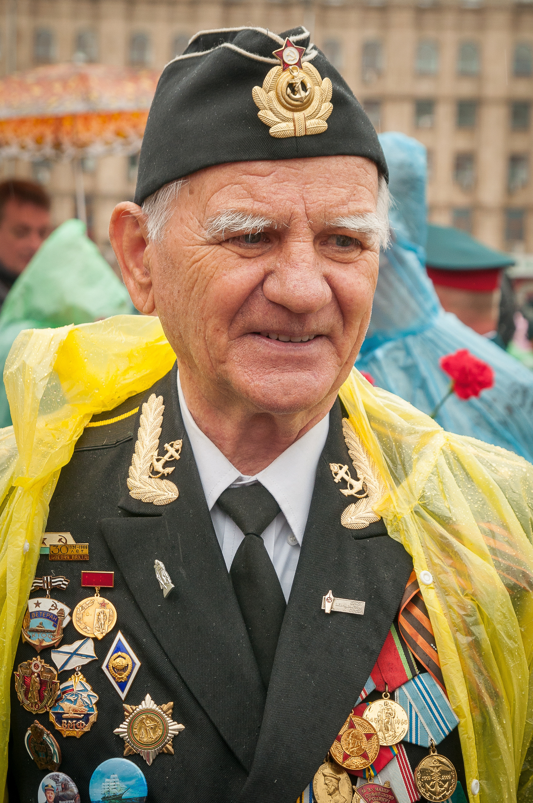 Ветеран с орденами в пилотке и жёлтом дождевике