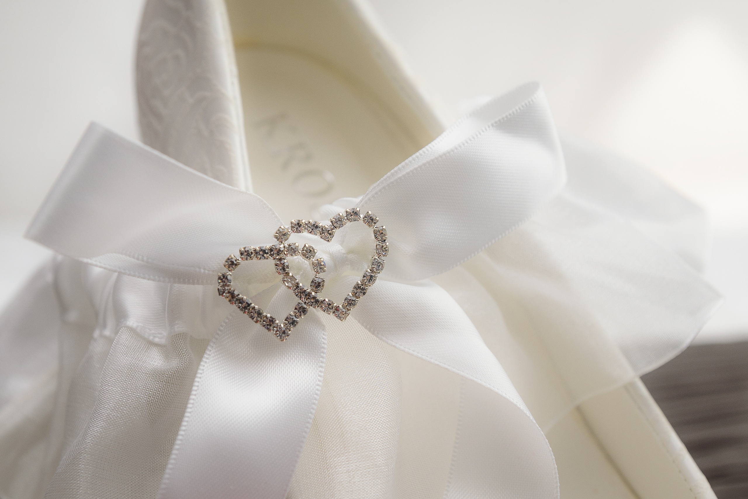 Белый бант с украшениями в виде сердец лежит на туфле невесты
