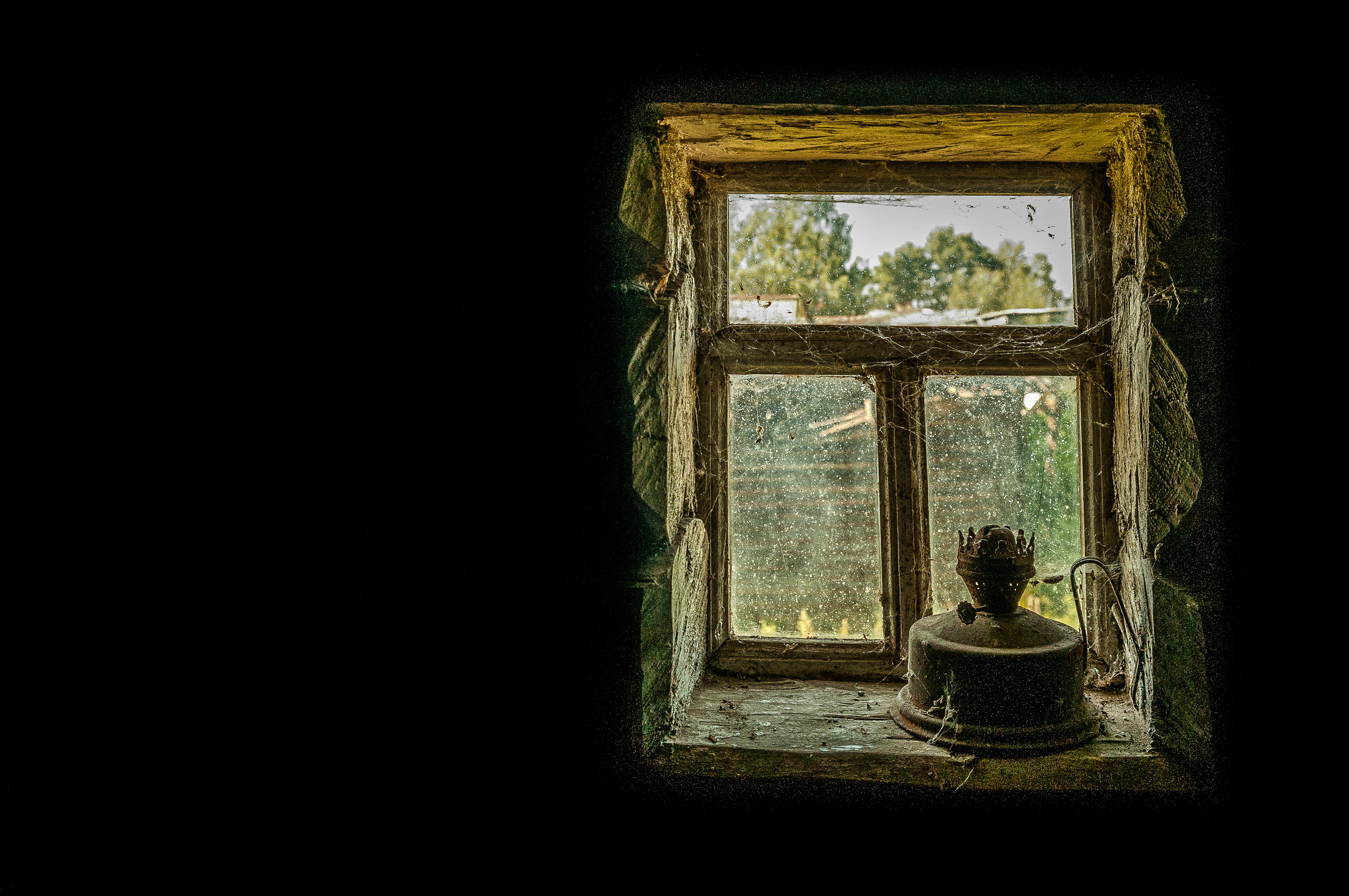 Старая керосиновая лампа стоит на окне, затянутом паутиной