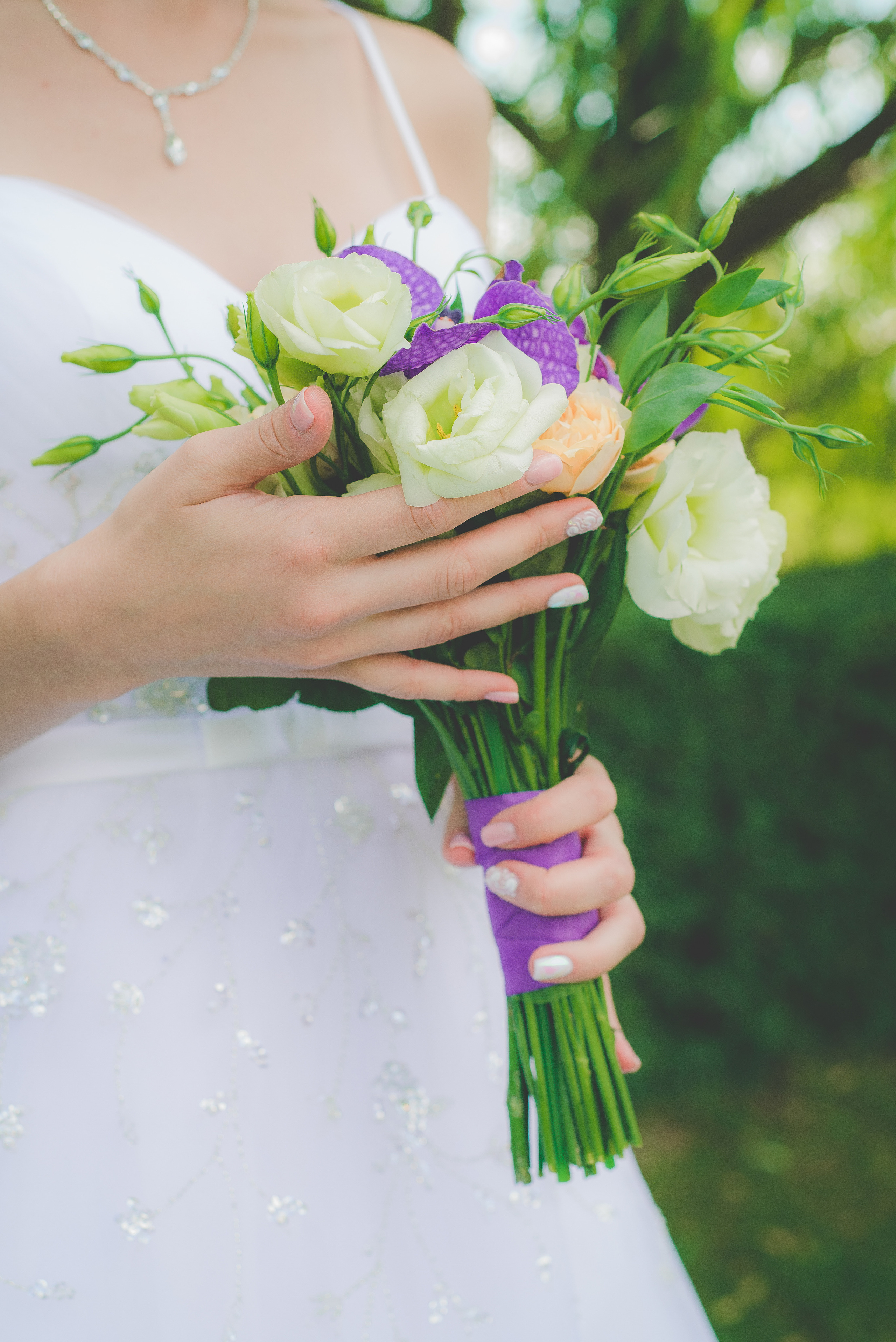 Невеста держит в руках свадебный букет с фиолетовыми и белыми цветами