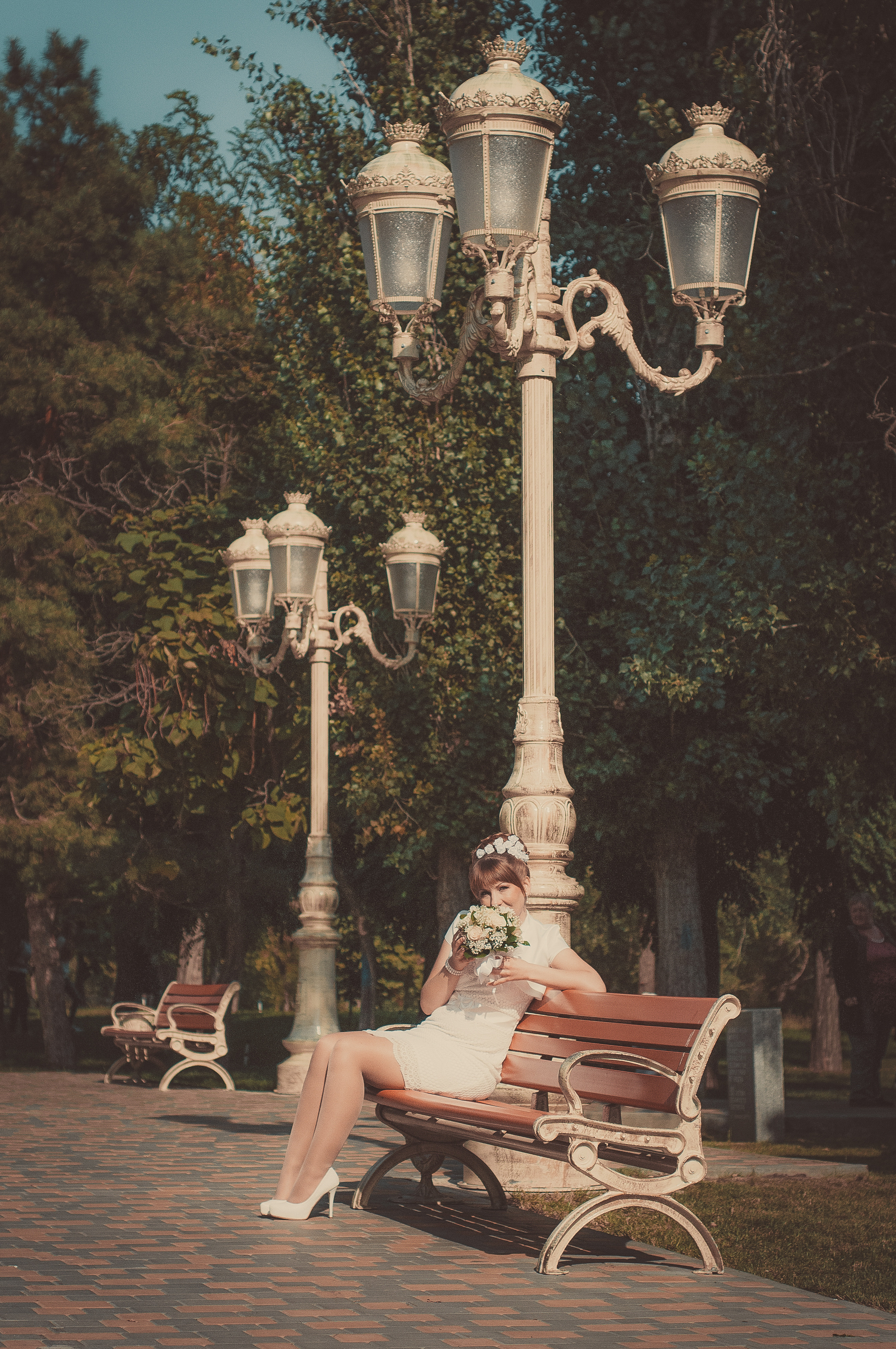 Невеста сидит на скамье под фонарём в парке