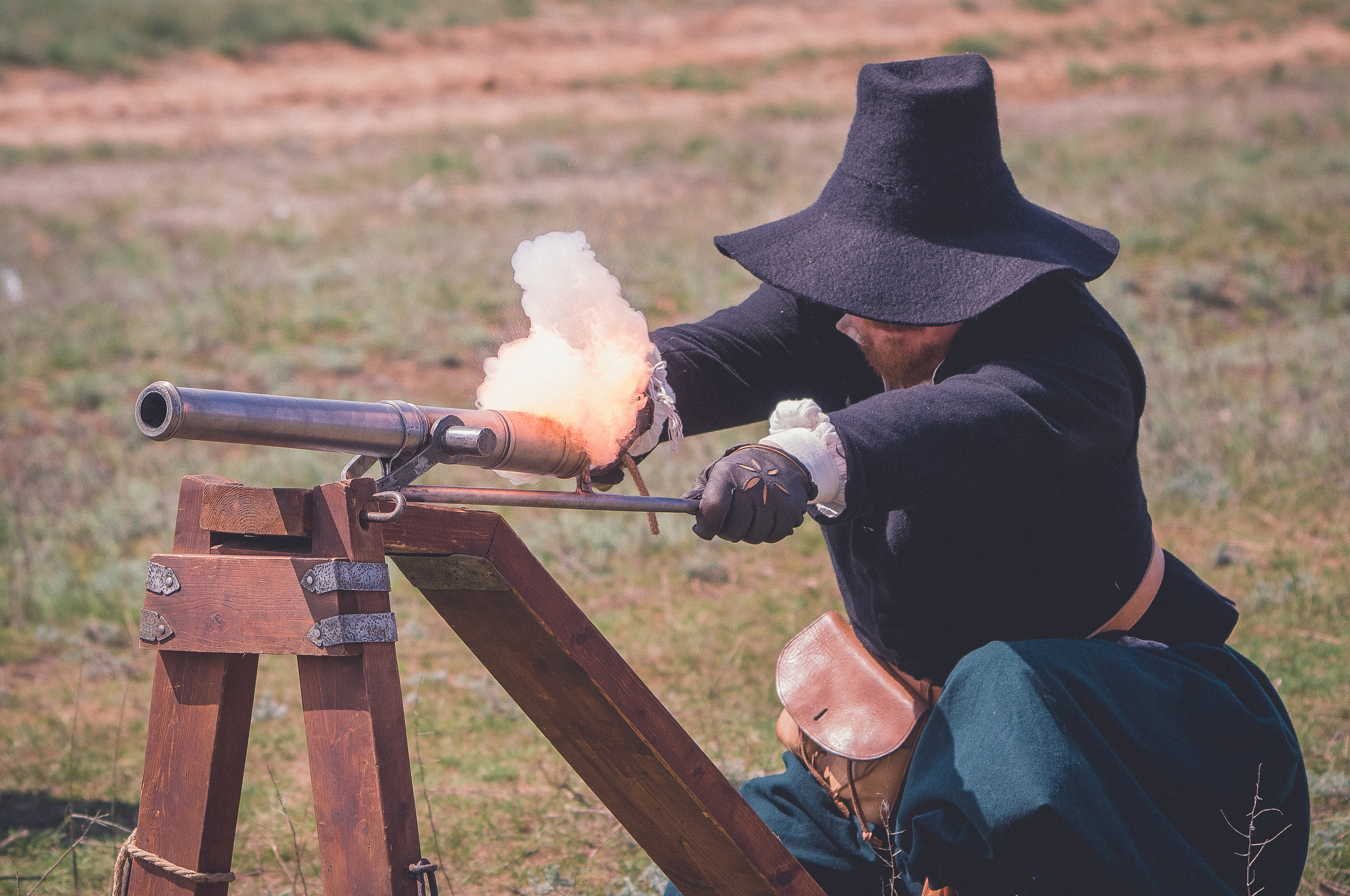 Реконструктор в костюме и шляпе с полями стреляет из старинного ружья
