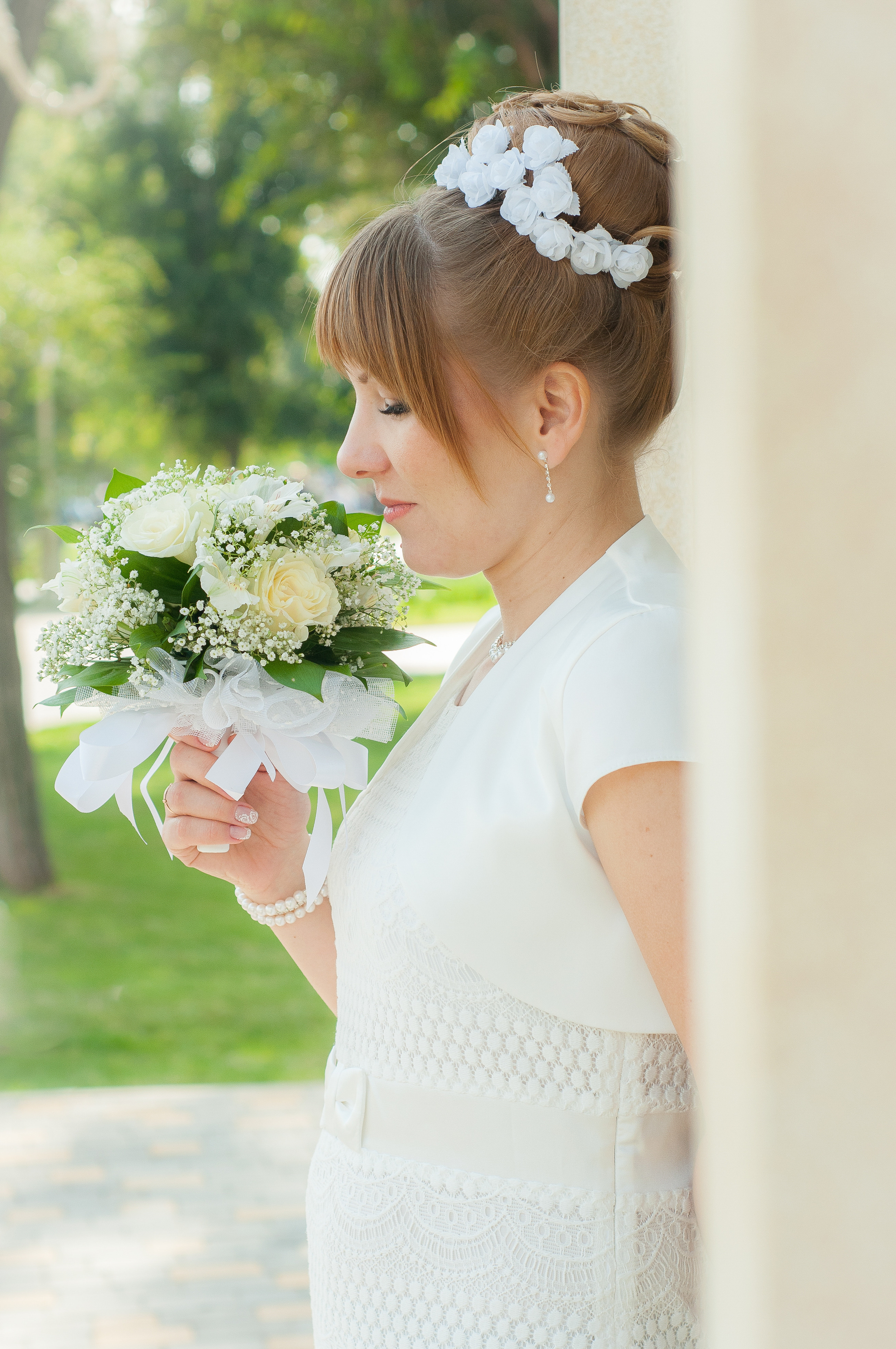 Невеста стоя у стены смотрит на свадебный букет