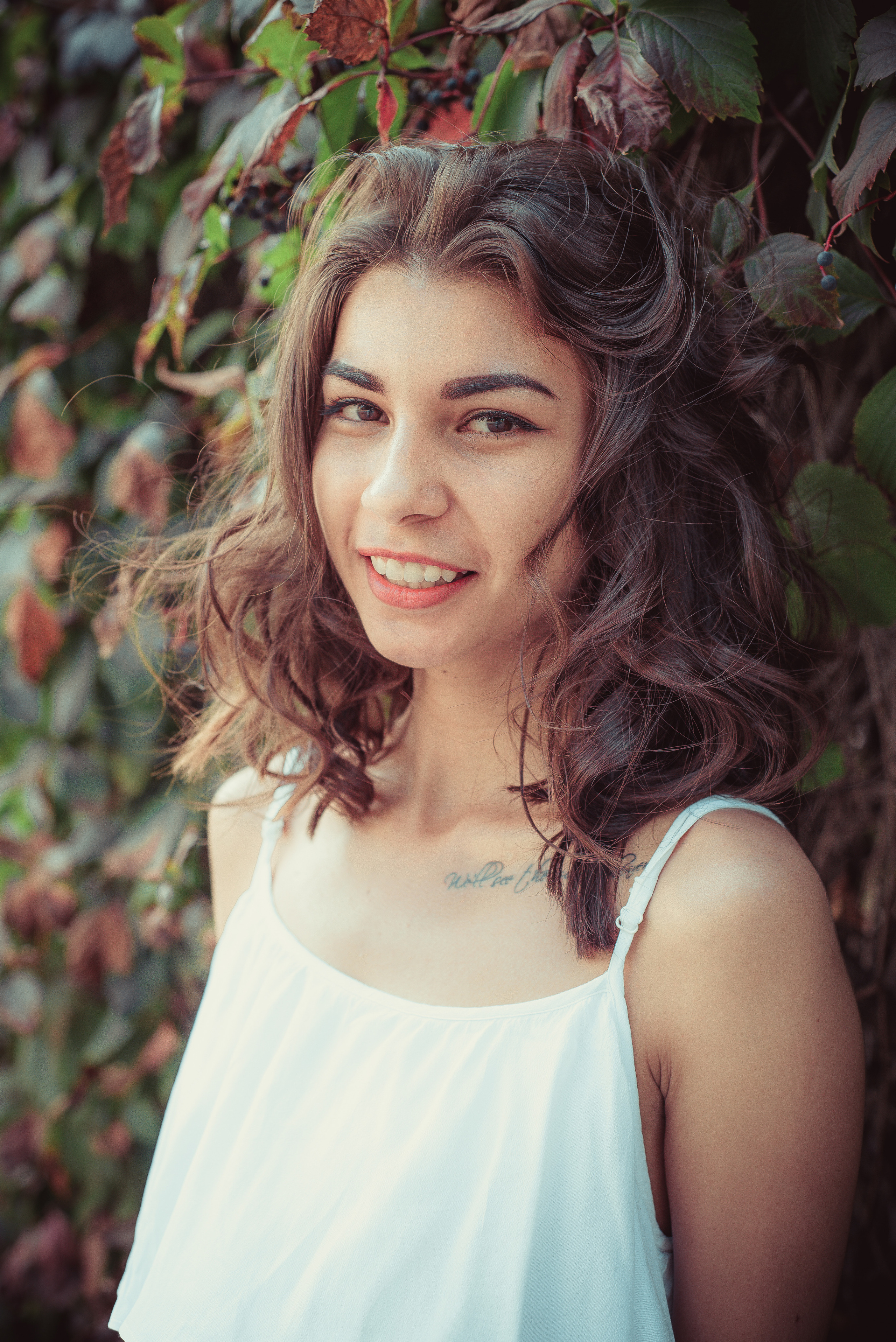 Девушка с кудрявыми волосами стоит у стены, заросшей виноградом