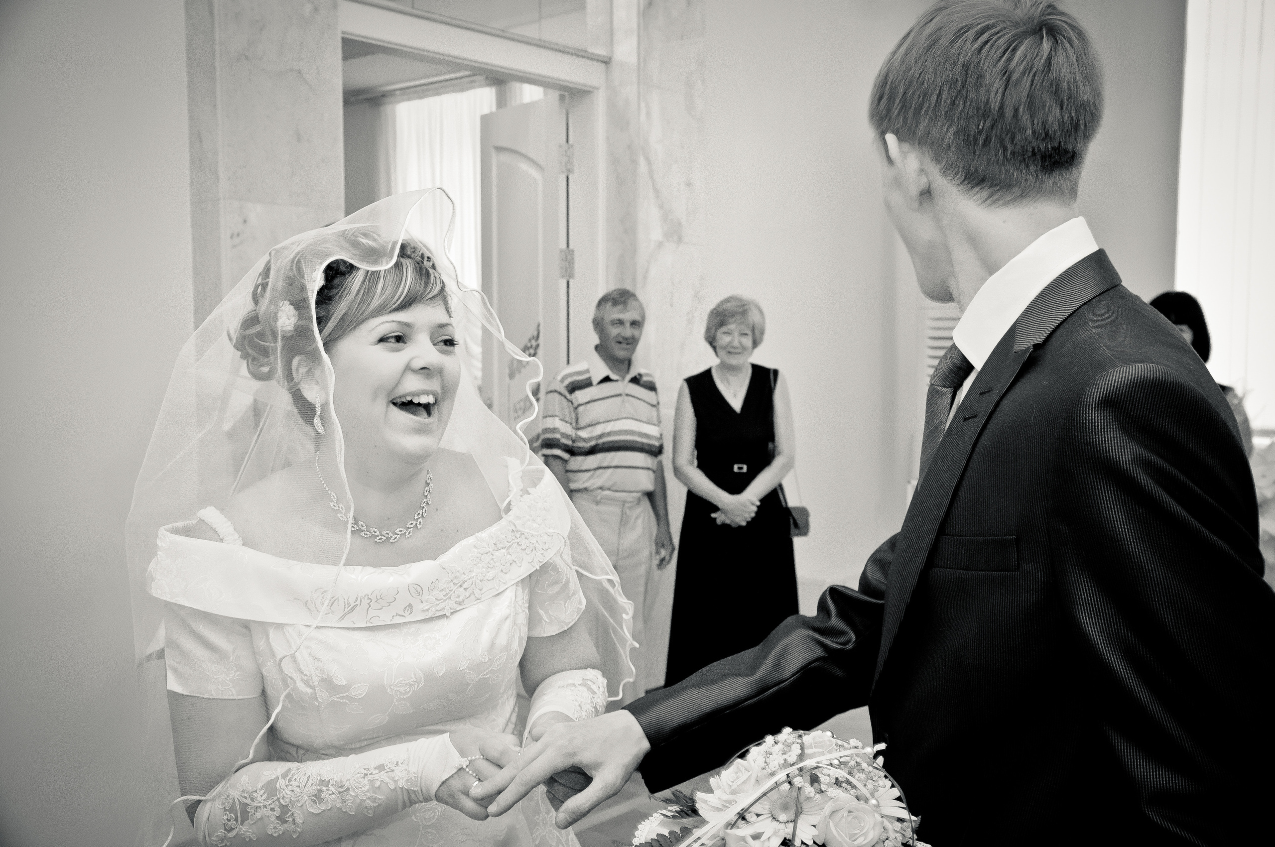 Невеста в ЗАГСе смеется, надевая кольцо жениху на палец