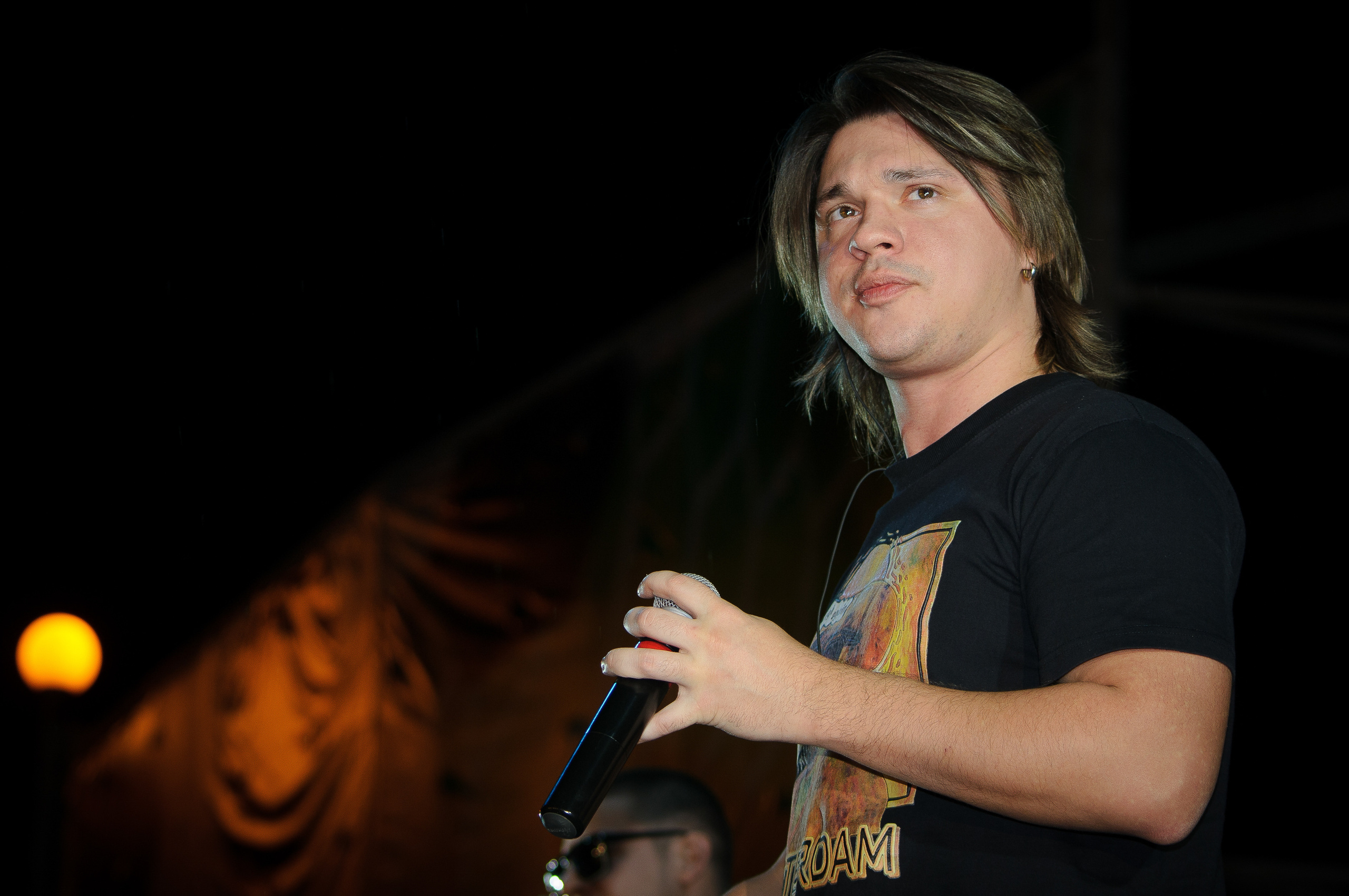 Участник группы Корни Алексей Кабанов в черной футболке на концерте с микрофоном в руке