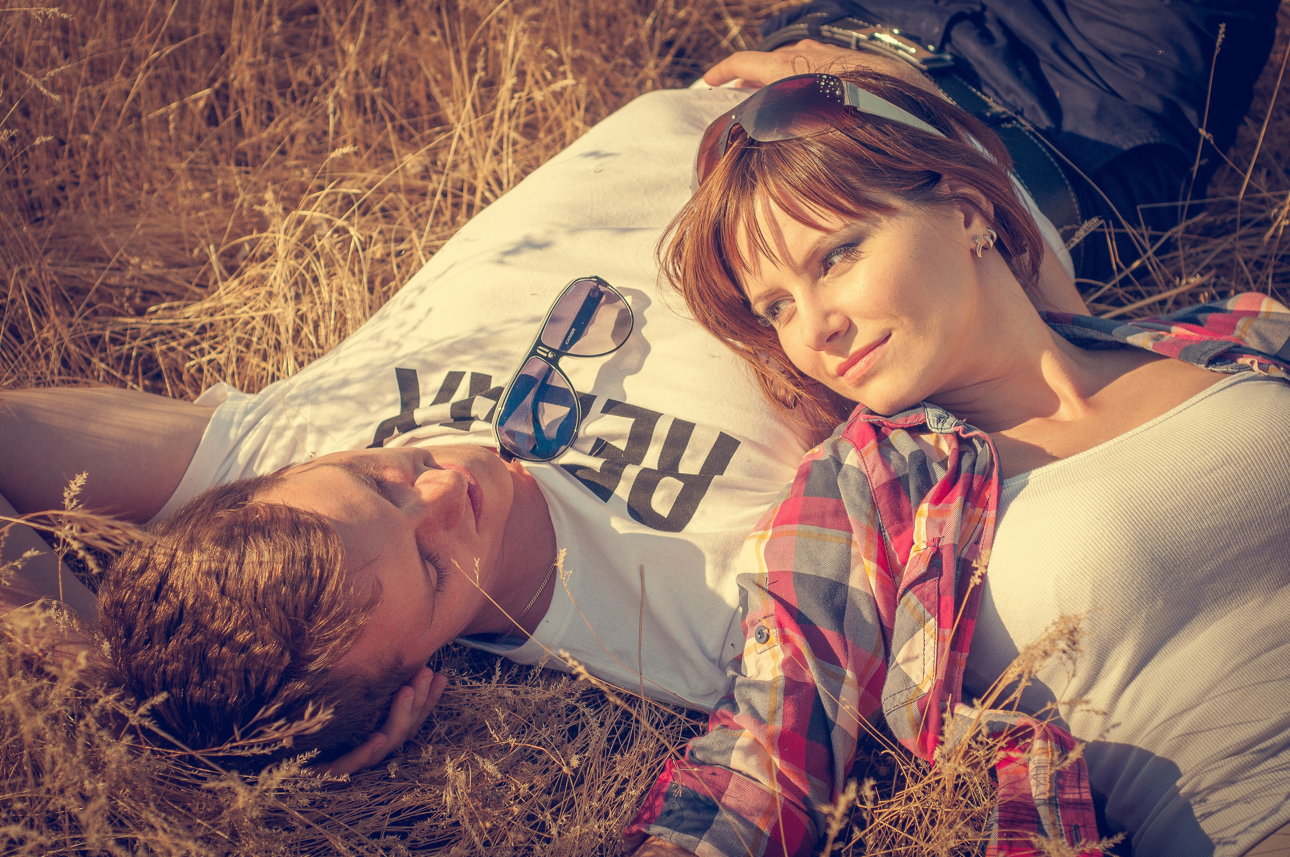 Парень с девушкой смотрят друг на друга лежа в траве на летнем лугу