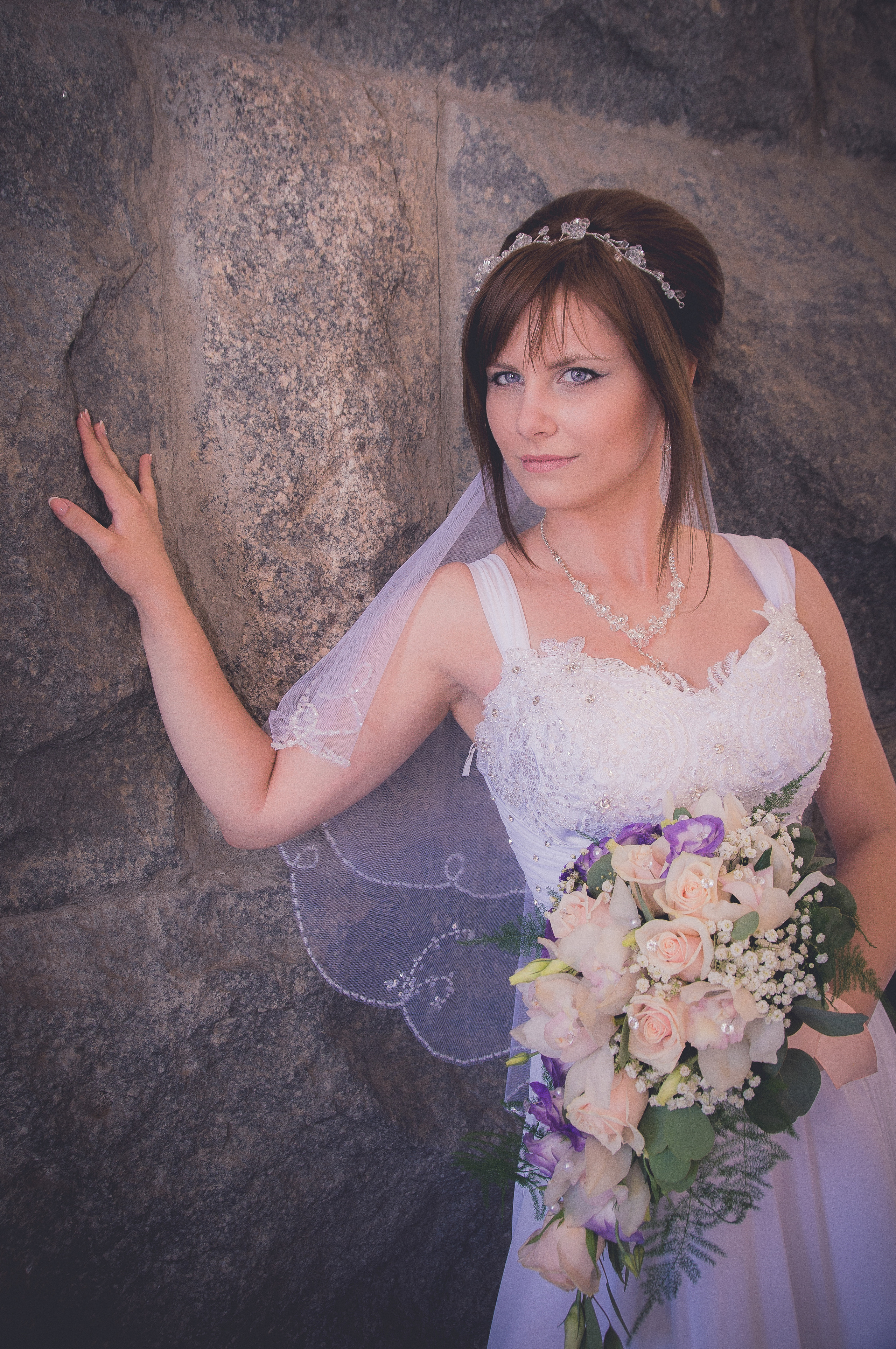 Невеста с букетом стоит у каменной стены