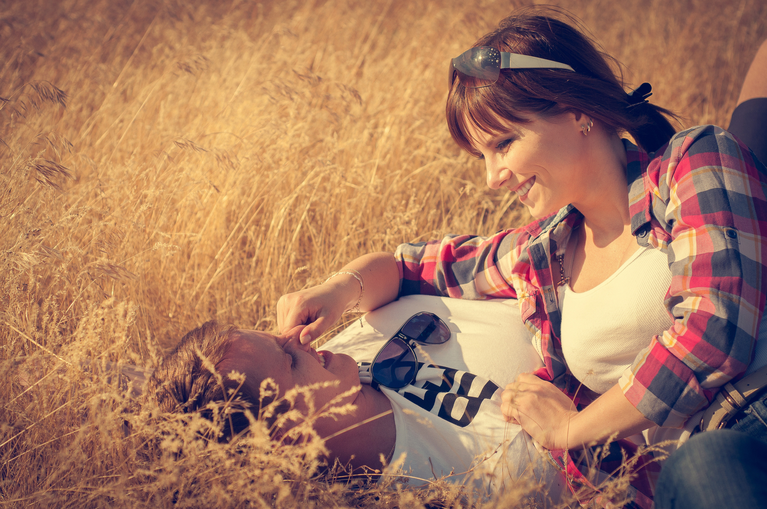 Влюбленная пара лежит в летнем поле, смотрит друг на друга и смеется