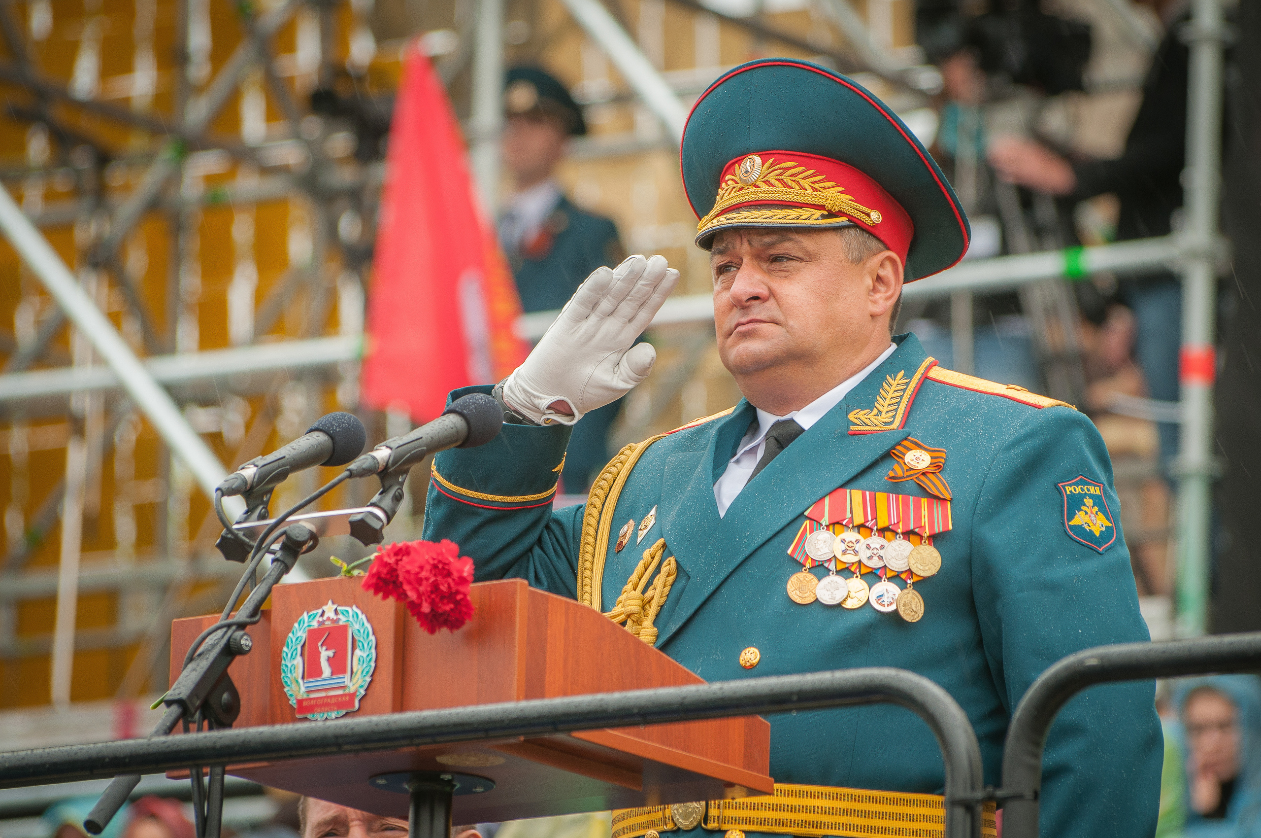 Командующий парадом генерал с наградами отдаёт честь стоя в парадном автомобиле