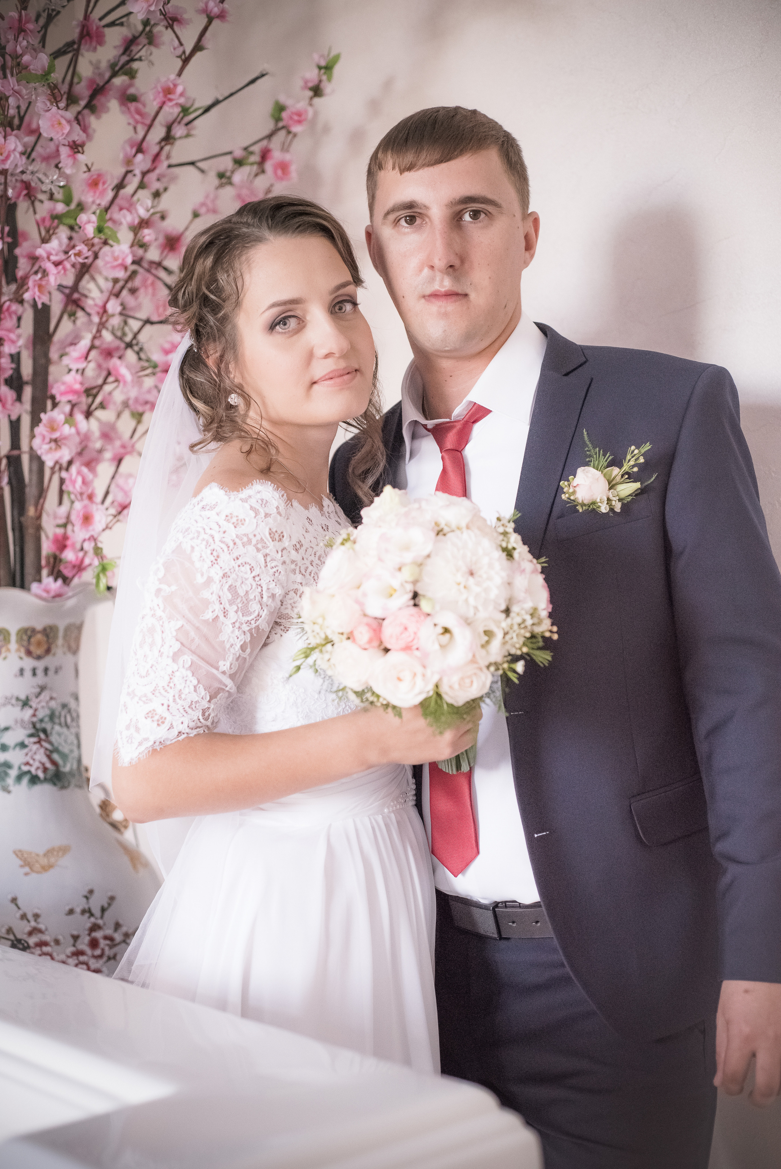 Жених и невеста с букетом в руках около розового дерева