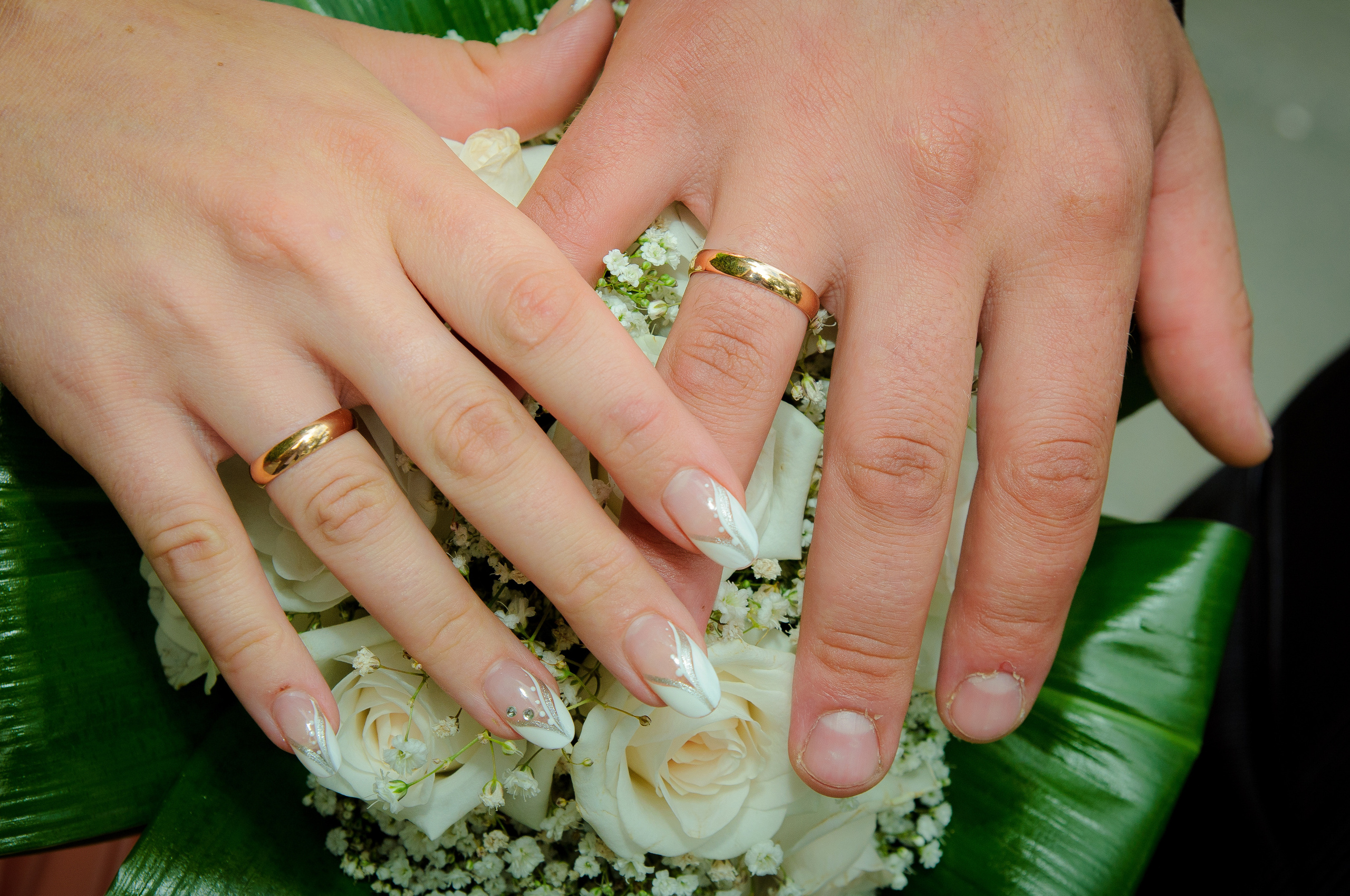 Руки жениха и невеста с обручальными кольцами на свадебном букете