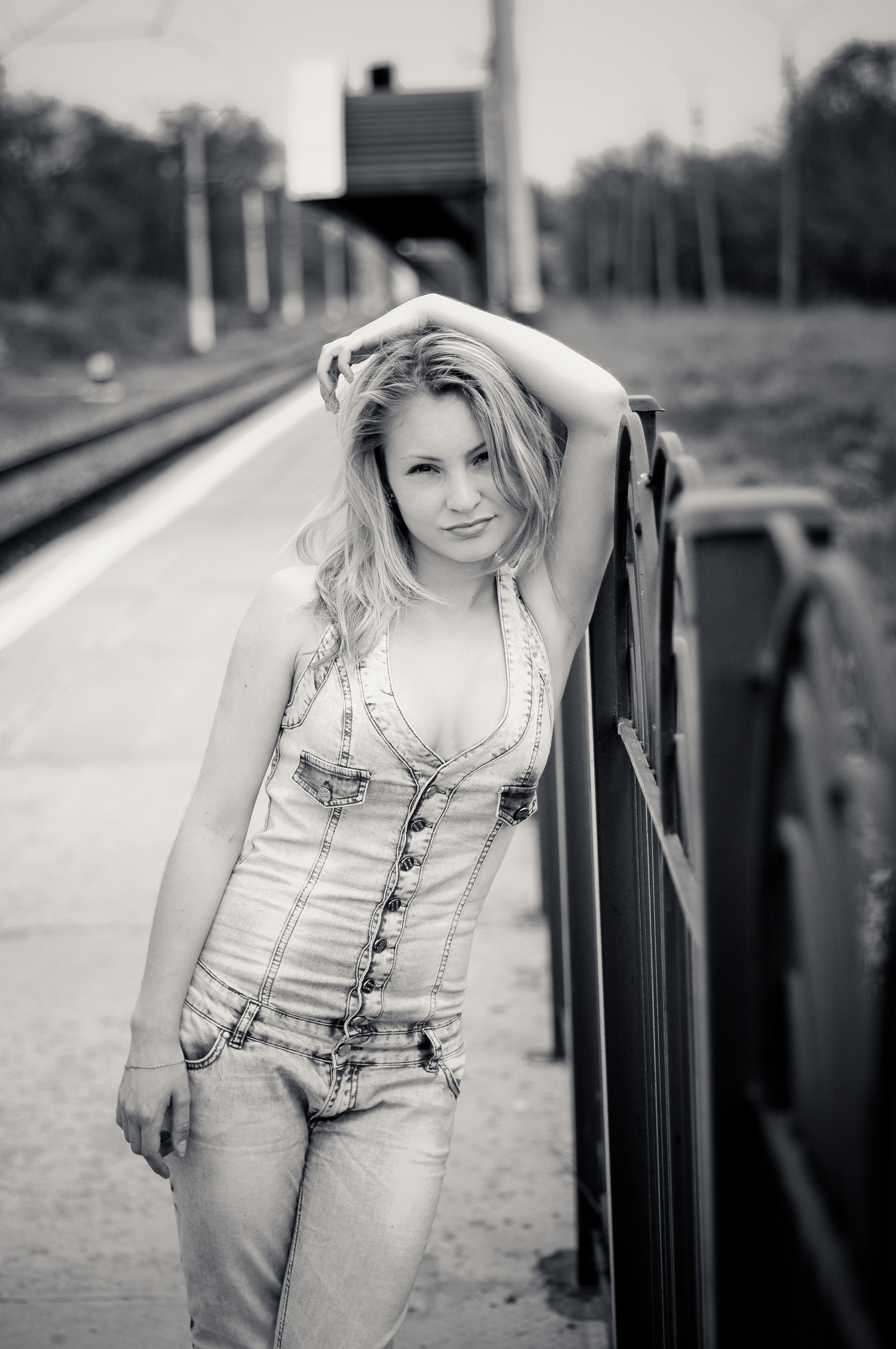 Девушка в джинсовой комбинезоне стоит на железнодорожной станции