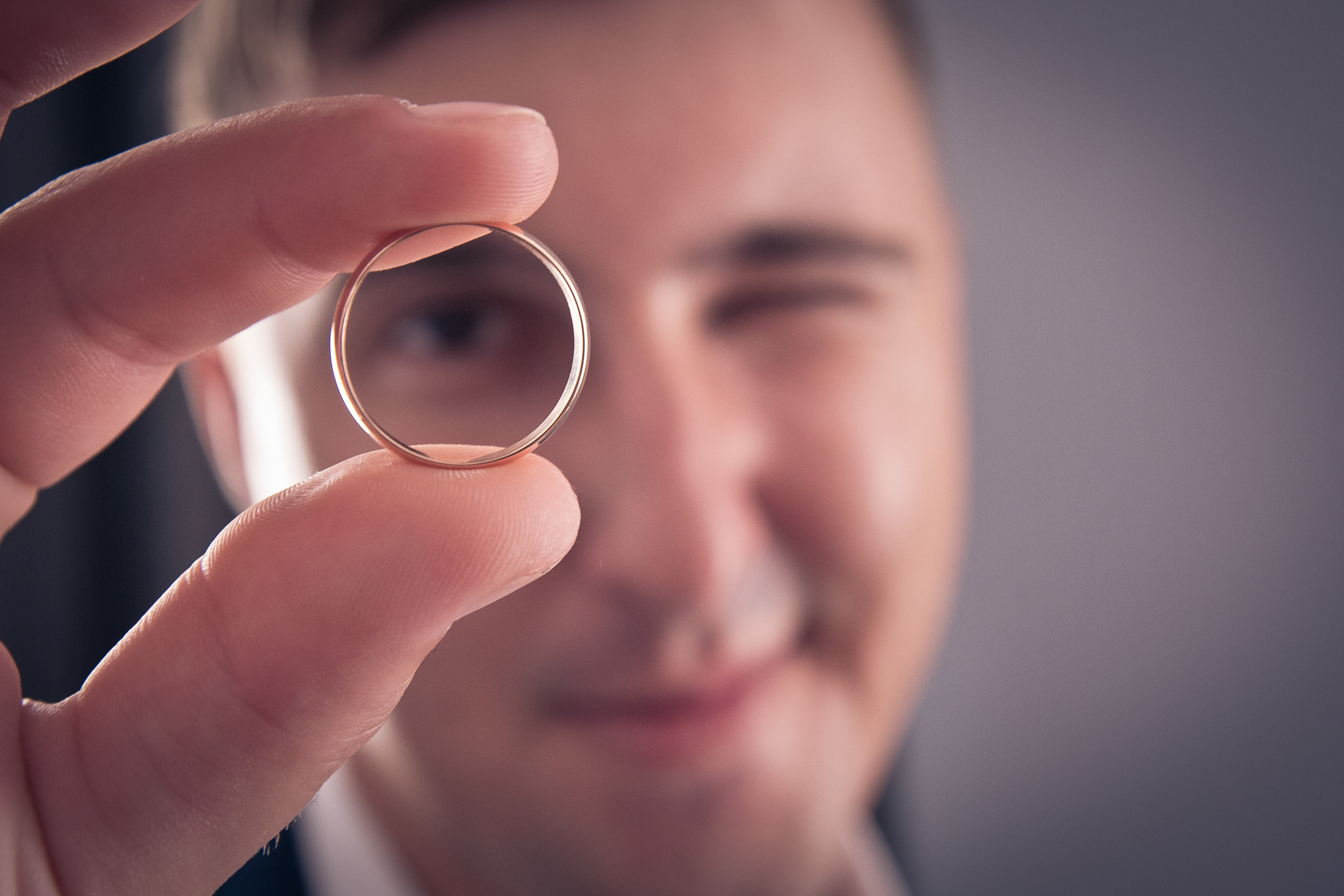 Жених смотрит сквозь свадебное кольцо, которое держит в руке