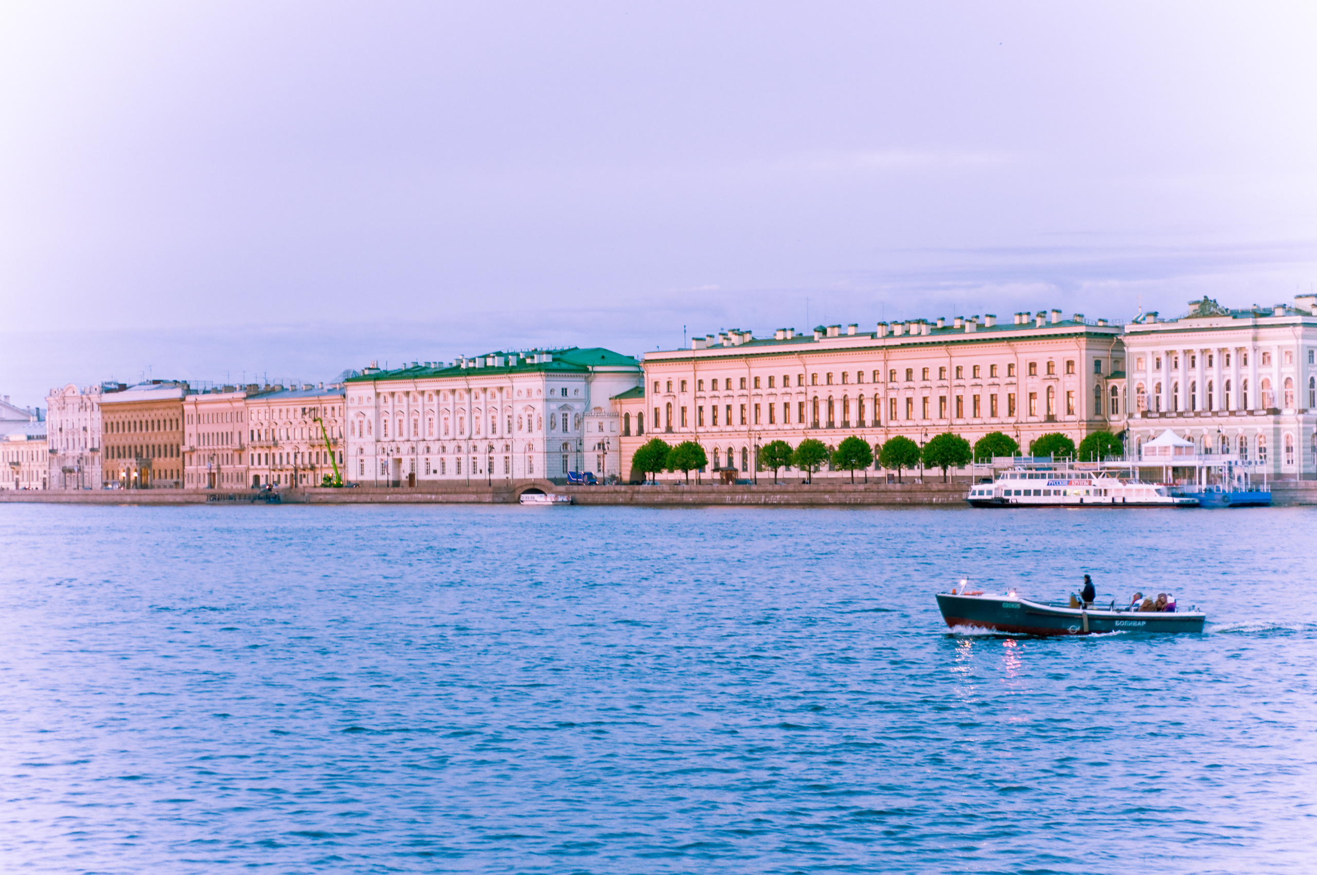 Небольшая лодка плывёт по Неве на фоне зданий Дворцовой набережной Санкт-Петербурга