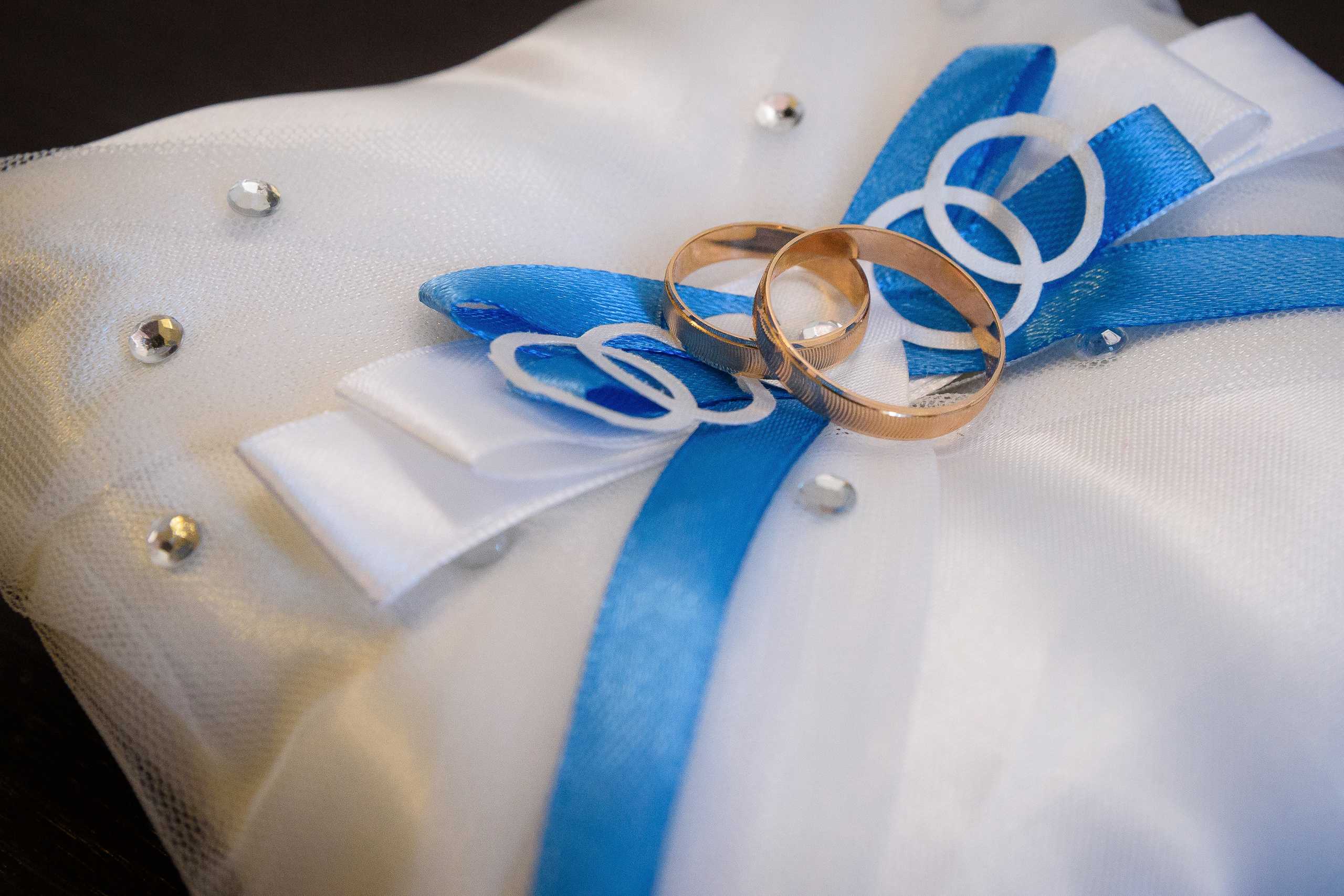 Обручальные кольца лежат на подушке с голубым бантом