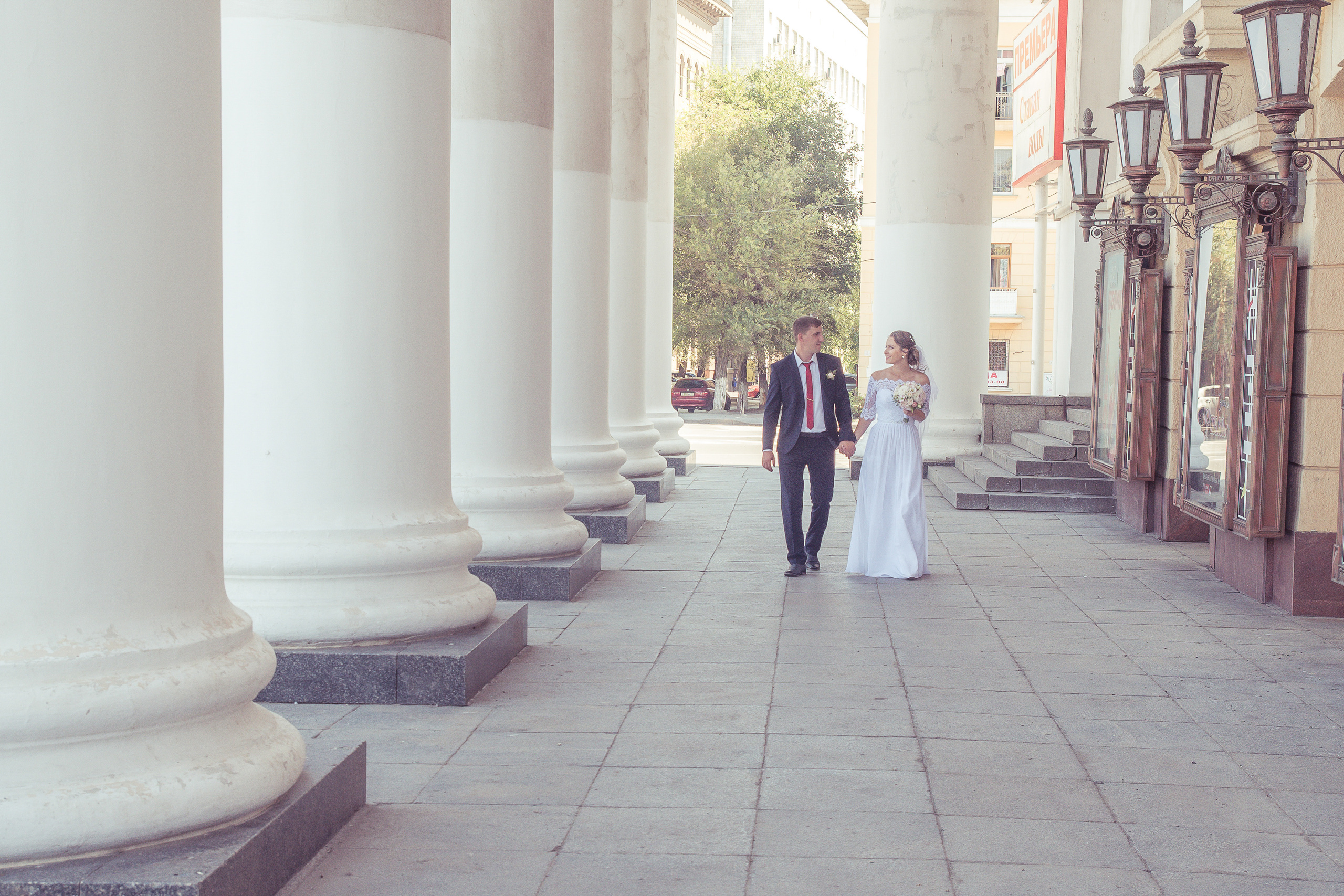 Жених и невеста идут вдоль больших колонн здания