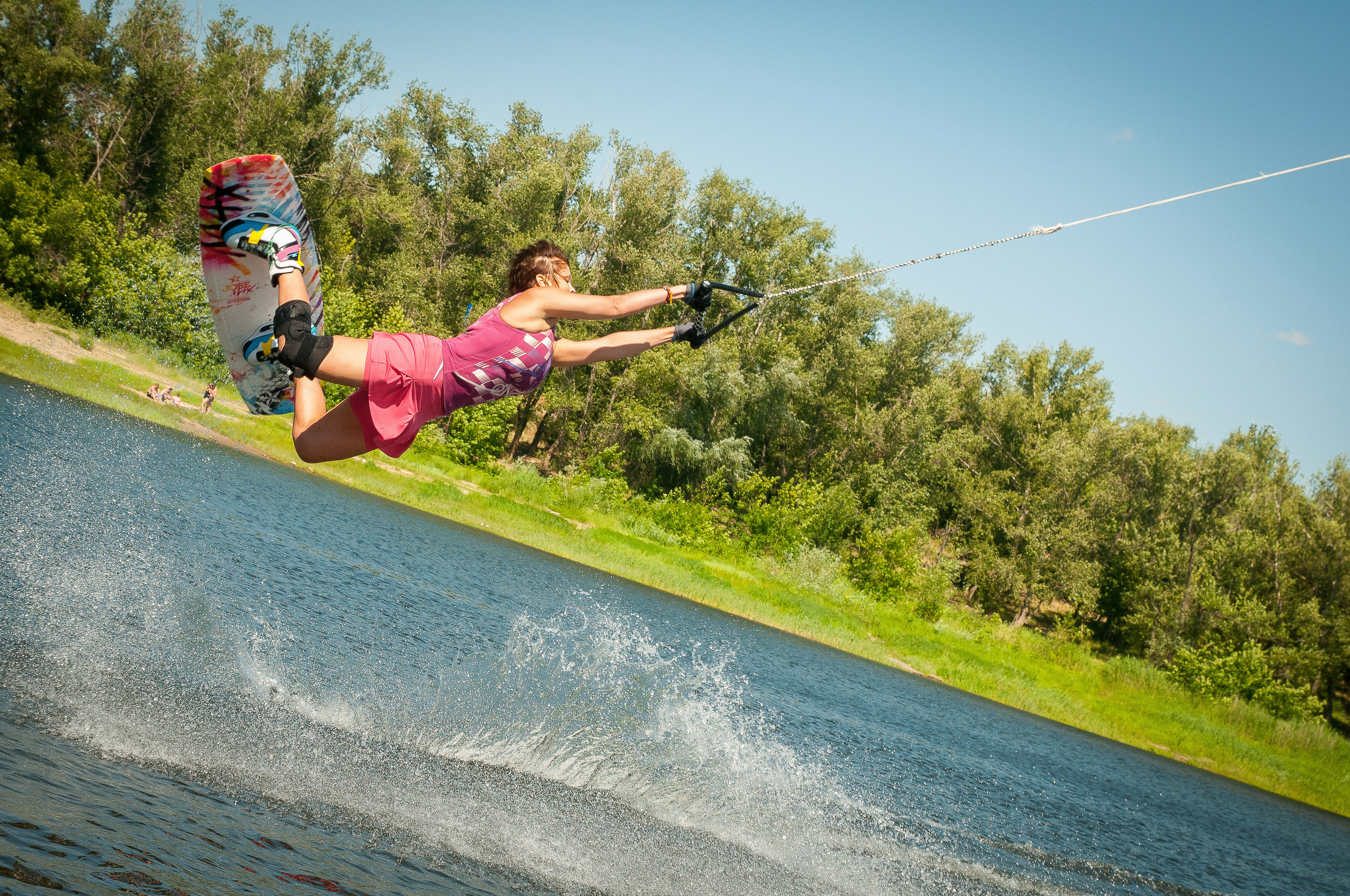 Девушка-вейкбордистка в розовом костюме летит в воздухе, схватившись за рукоятку