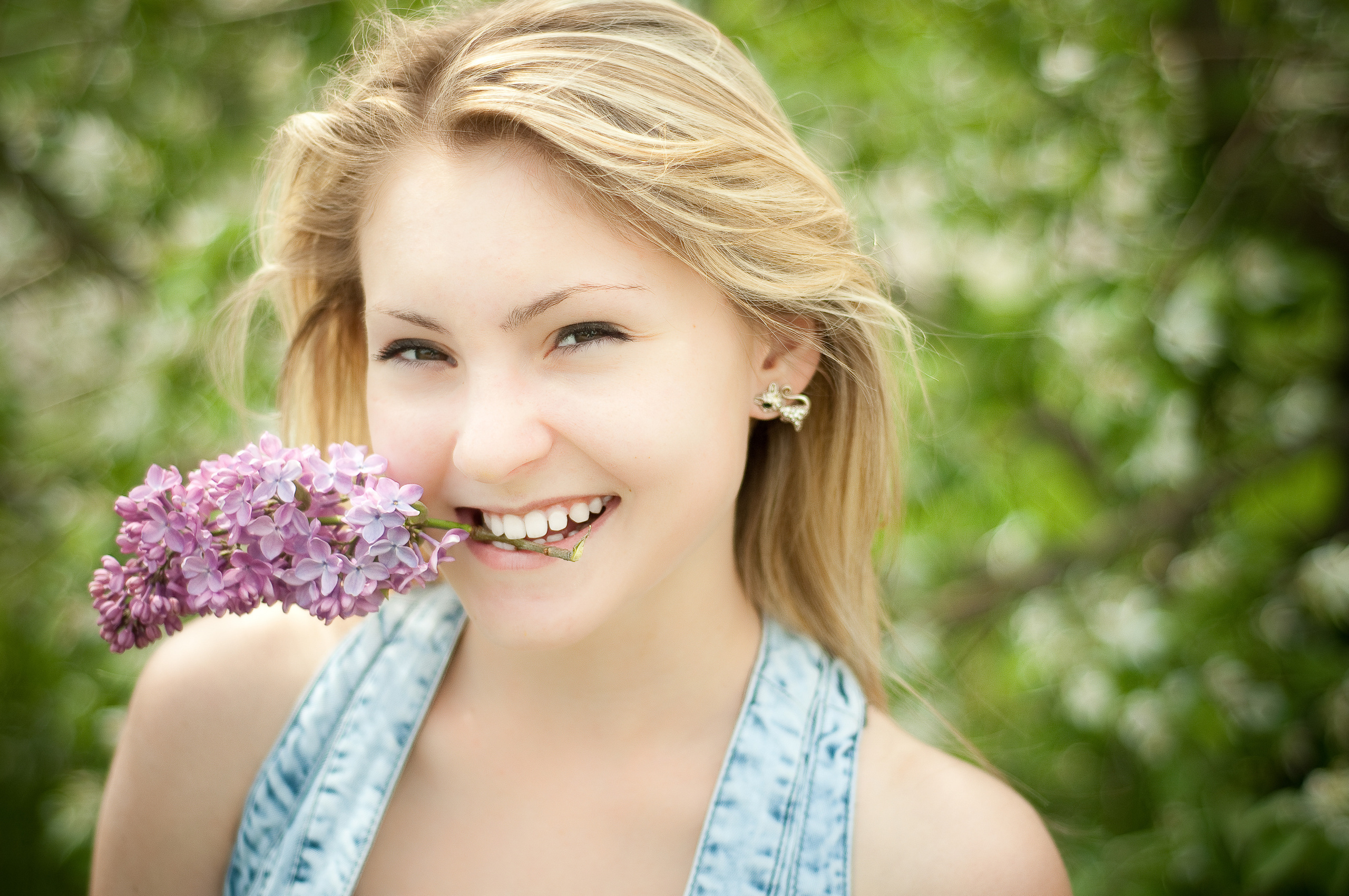 Улыбающаяся девушка с веткой сирени в зубах