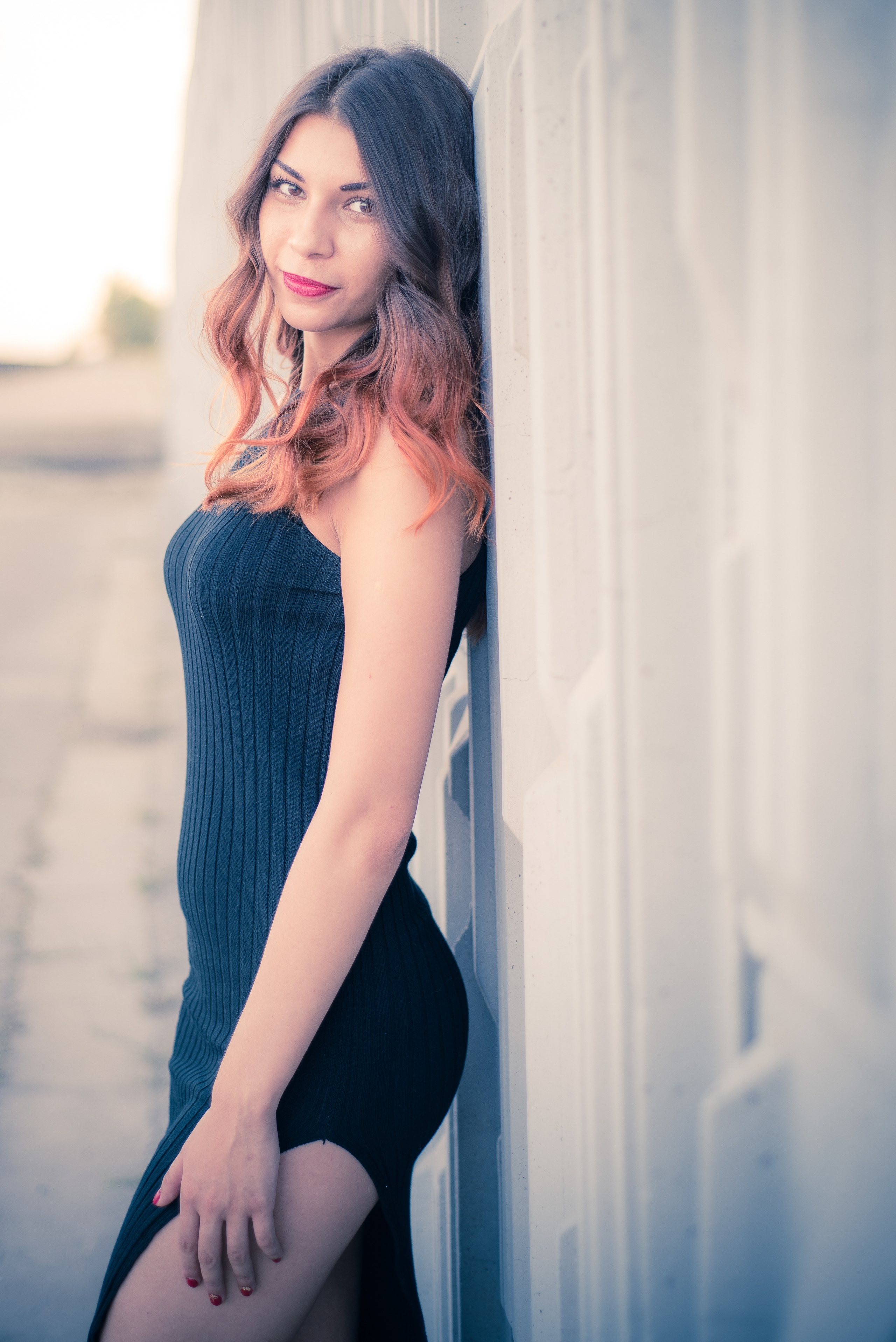 Девушка в облегающем платье стоит у стены дома