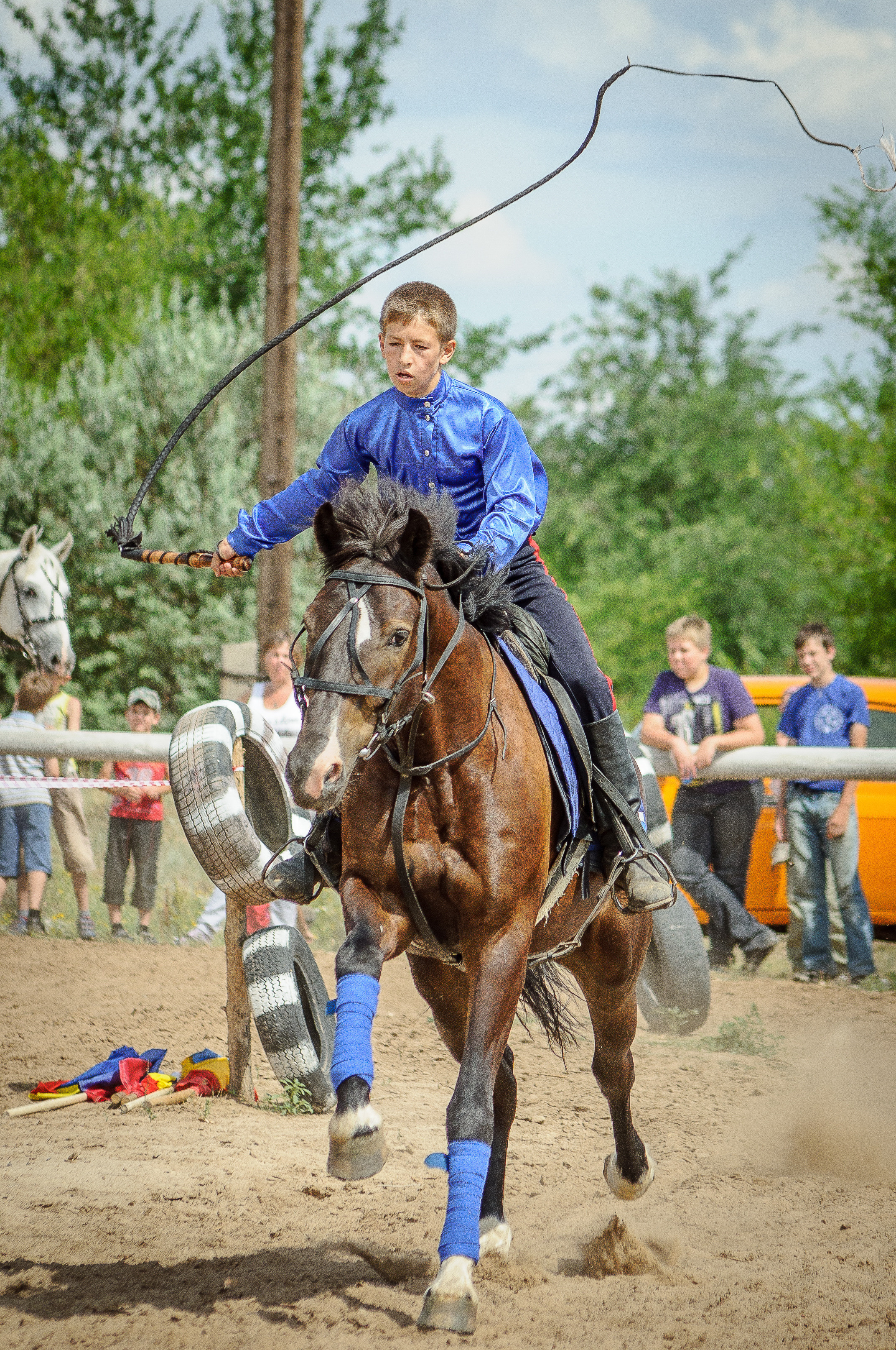 Мальчик в синей рубашке с кнутом скачет на коне