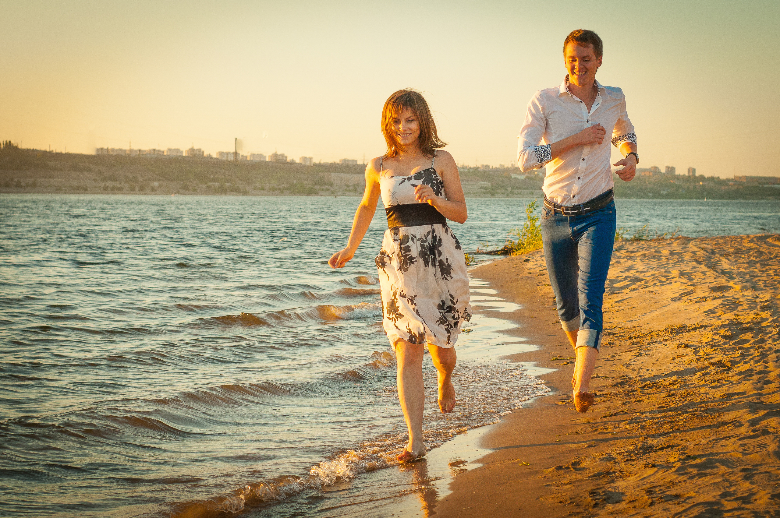 Парень и девушка бегут по берегу реки на закате