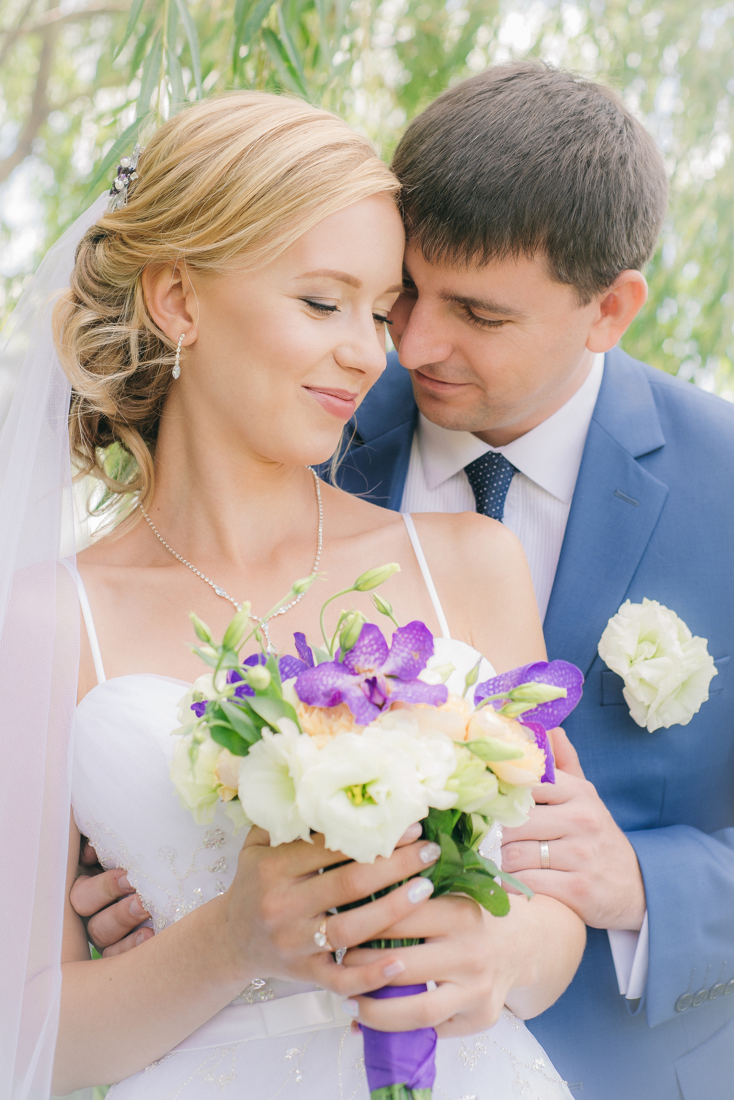 Жених обнимают сзади улыбающуюся невесту с букетом в руках