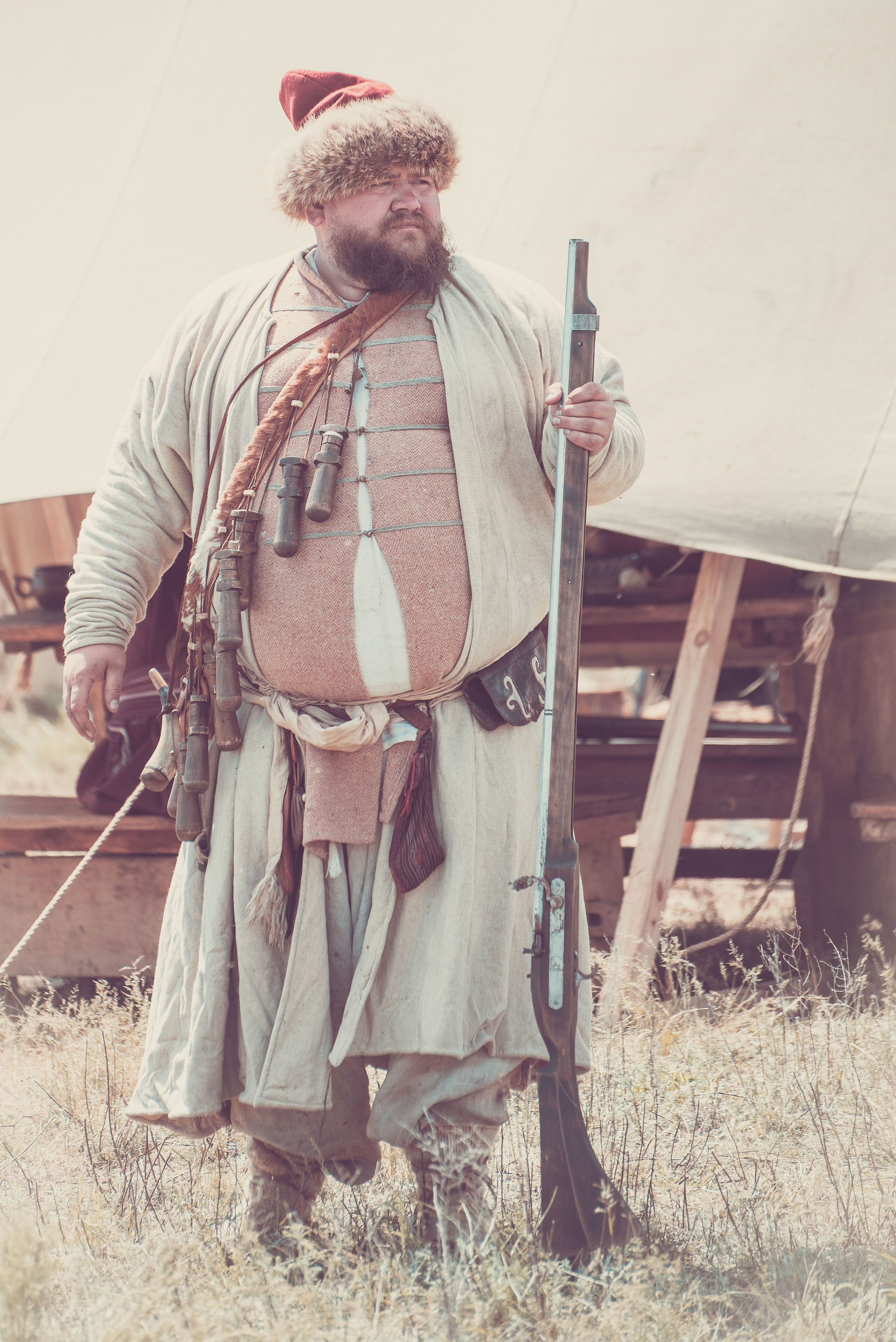 Мужчина в историческом костюме и шапке стоит со старинным ружьём 
