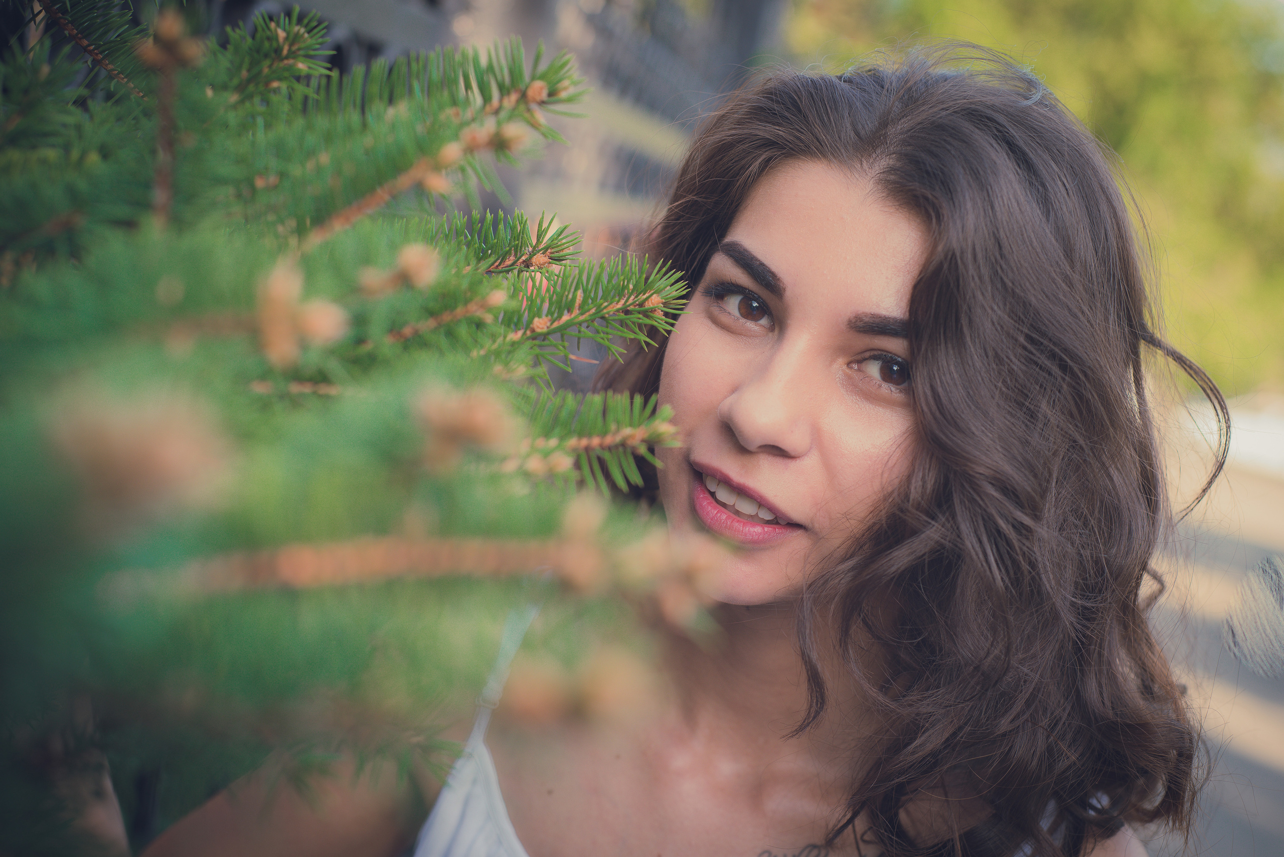 Девушка с кудрявыми волосами с ветками ели на переднем плане