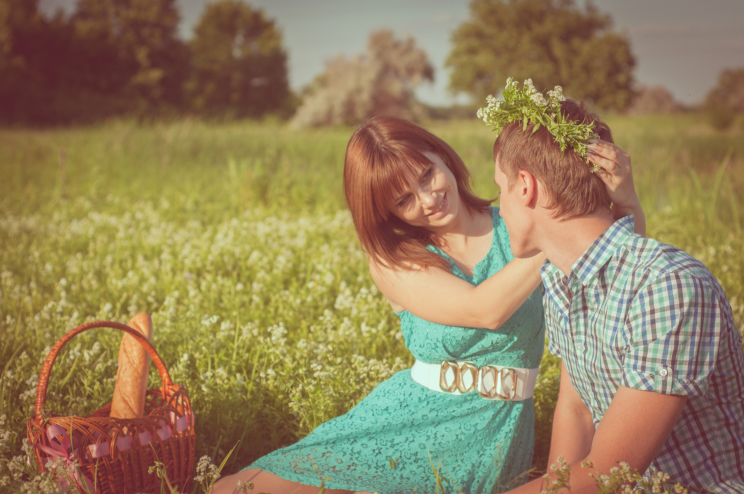 Девушка и парень сидят в траве, девушка надевает венок