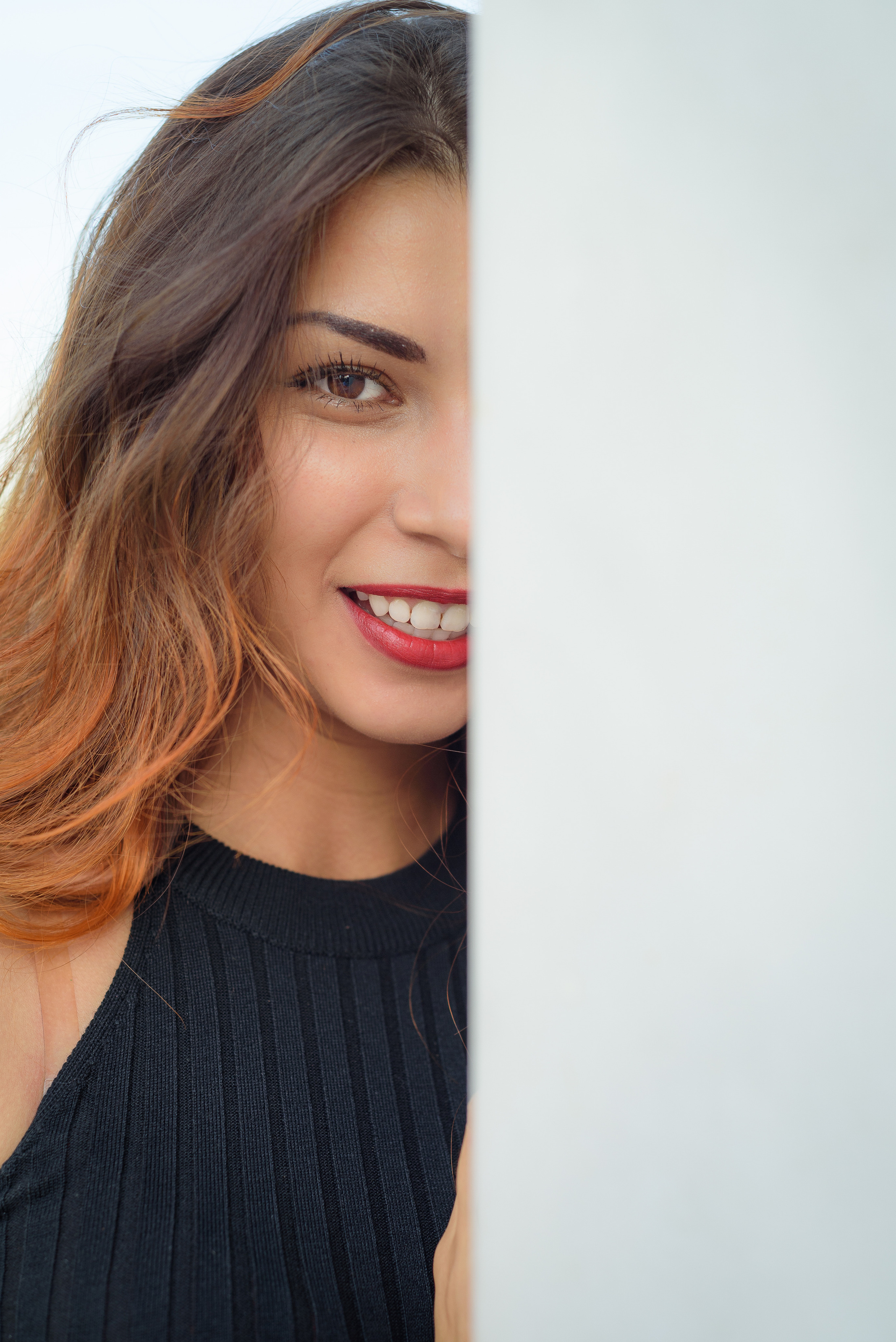 Девушка в черном платье и с красной помадой стоит около белой стены