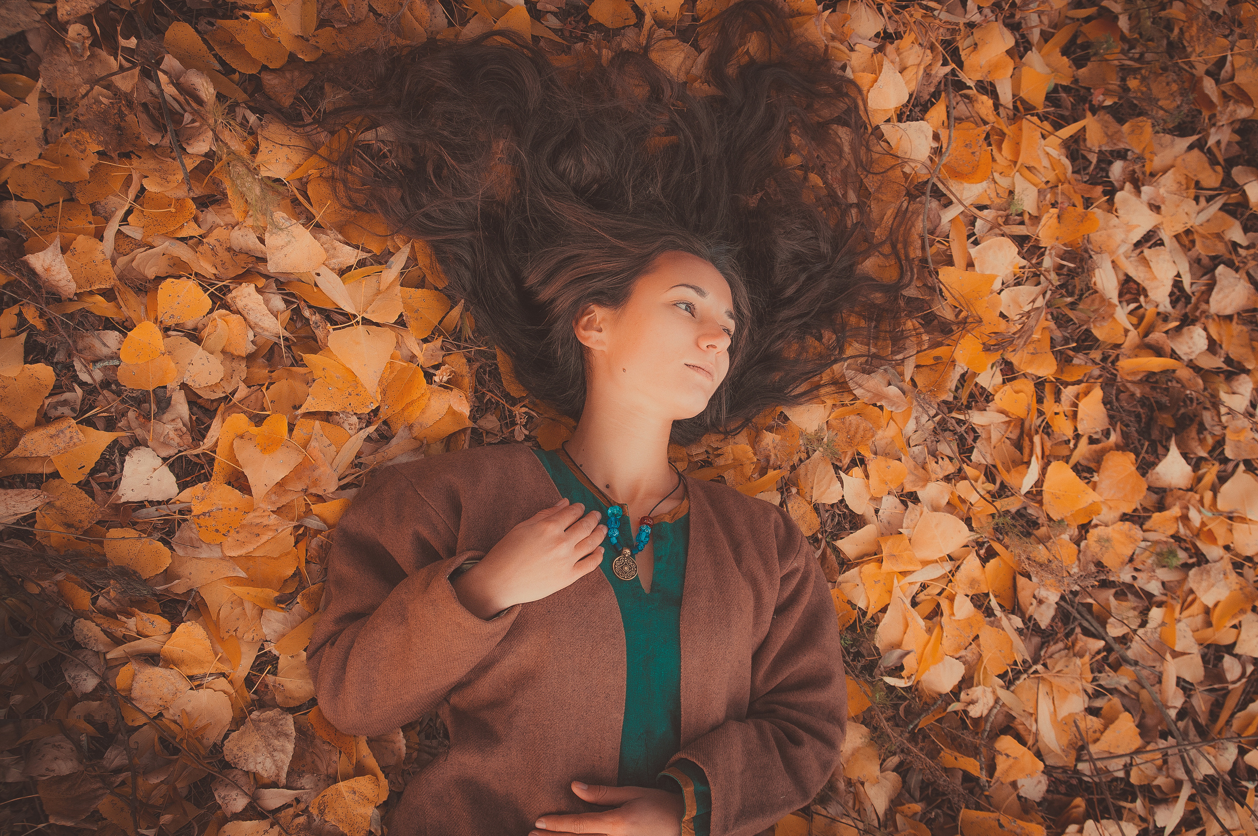 Девушка в коричневой одежде лежит на осенних листьях с распущенными волосами