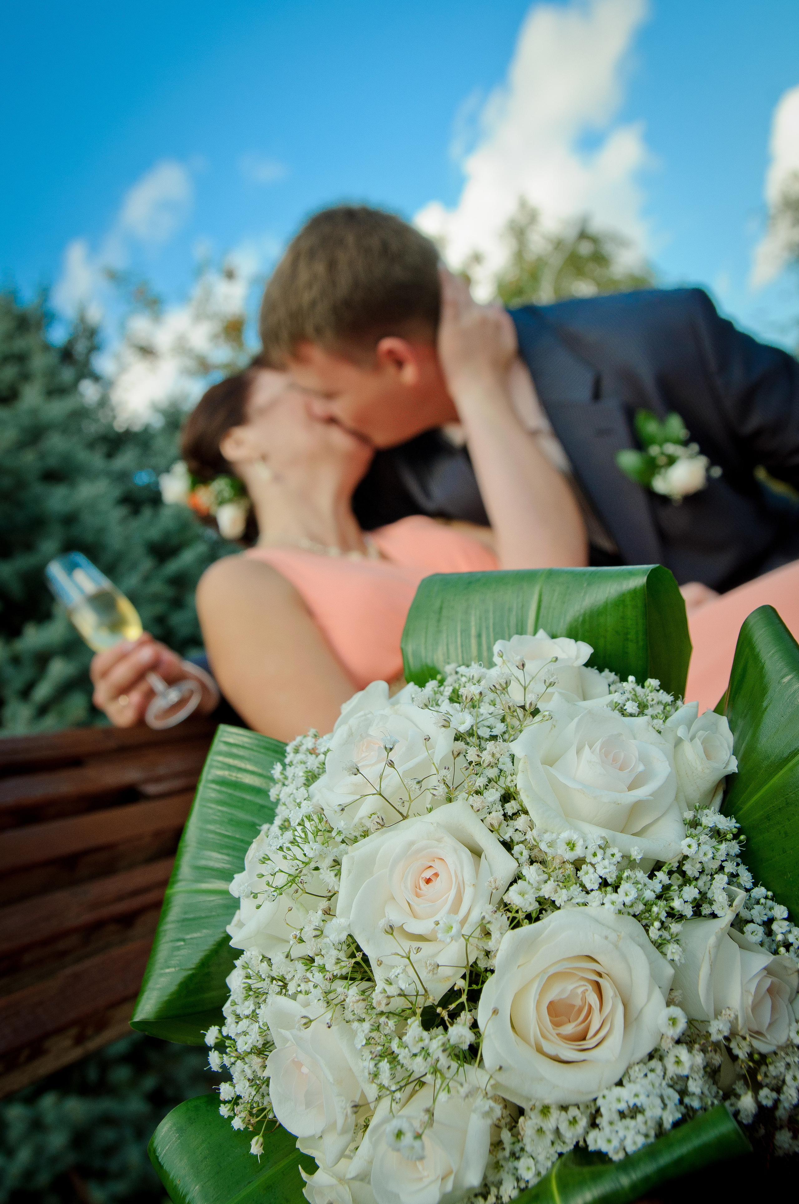 Свадебный букет из белых роз на фоне целующихся жениха и невесты