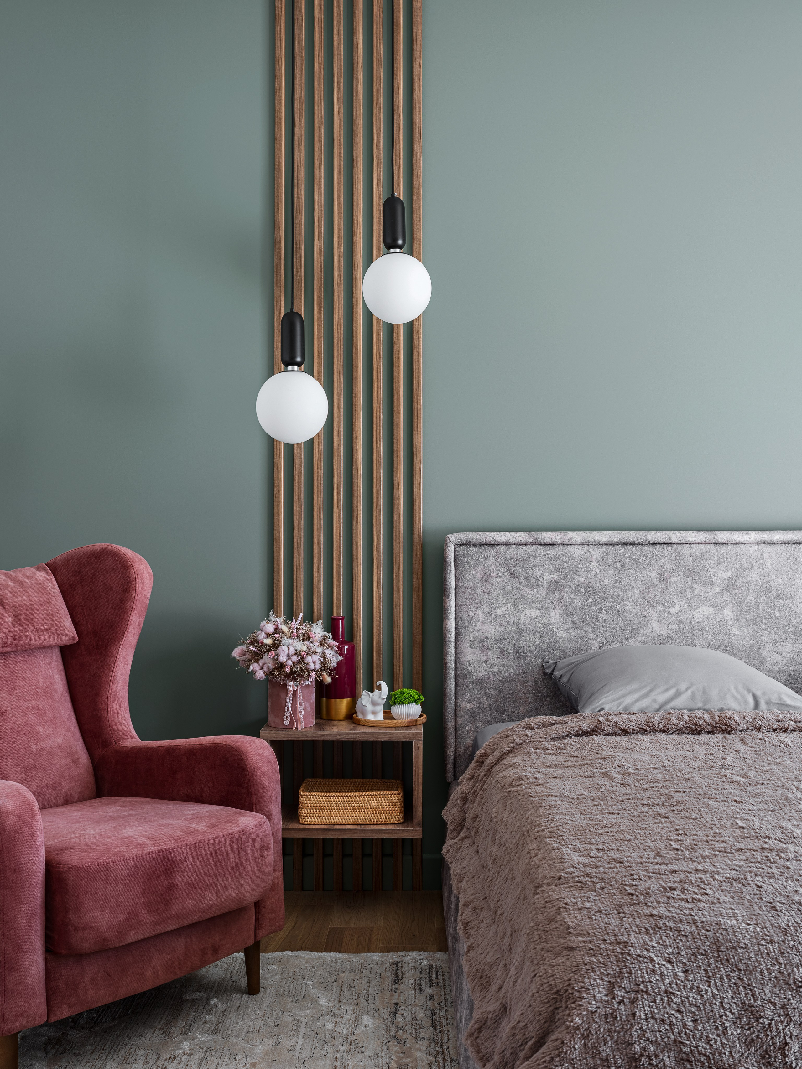 Деталь интерьера спальни: бордовое кресло, прикроватная тумба с цветами и подвесные светильники на фоне акцентной зелёной стены, дизайнерское решение Алёны Поповой и Анастасии Дмитриевой, фото Сергея Денисенко.