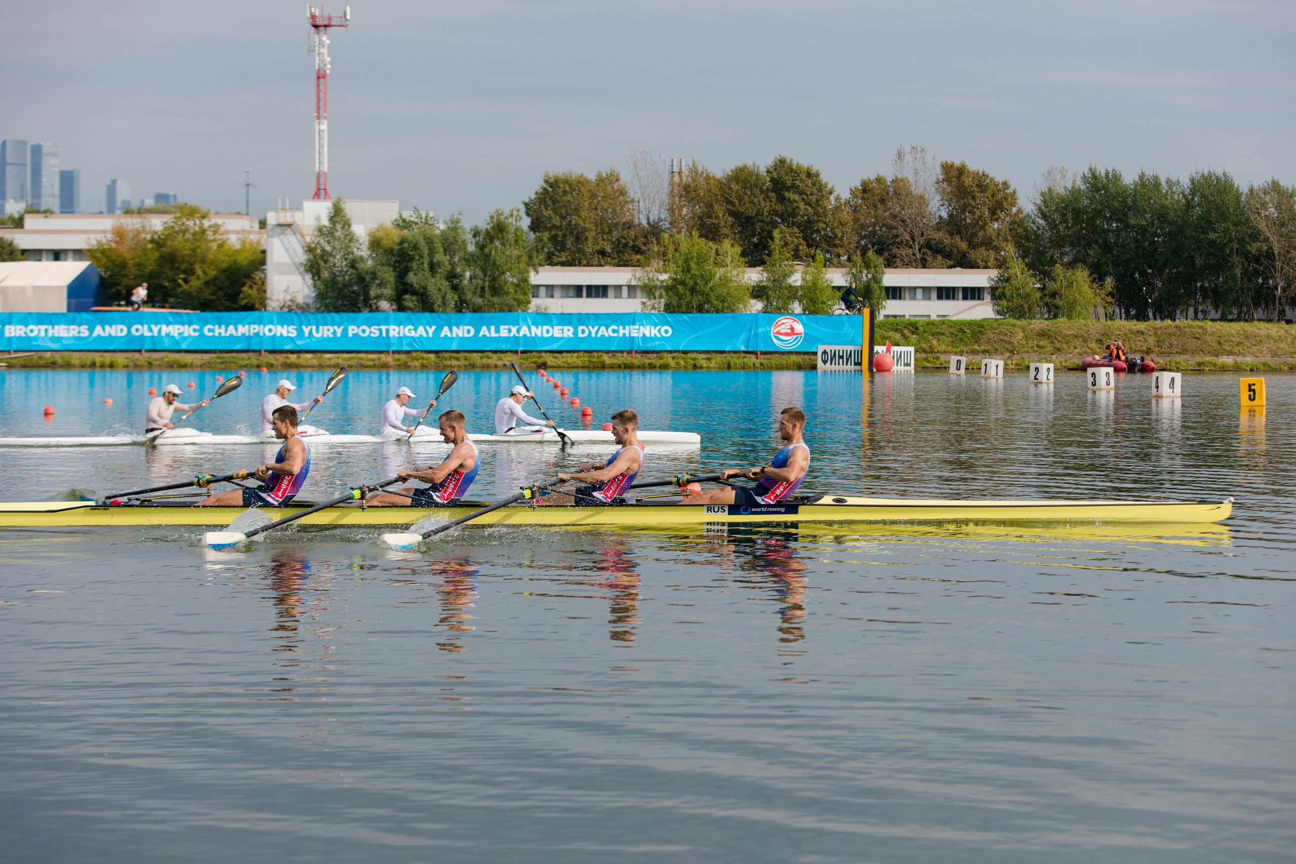 Четыре спортсмена сидят в байдарке и гребут в канале