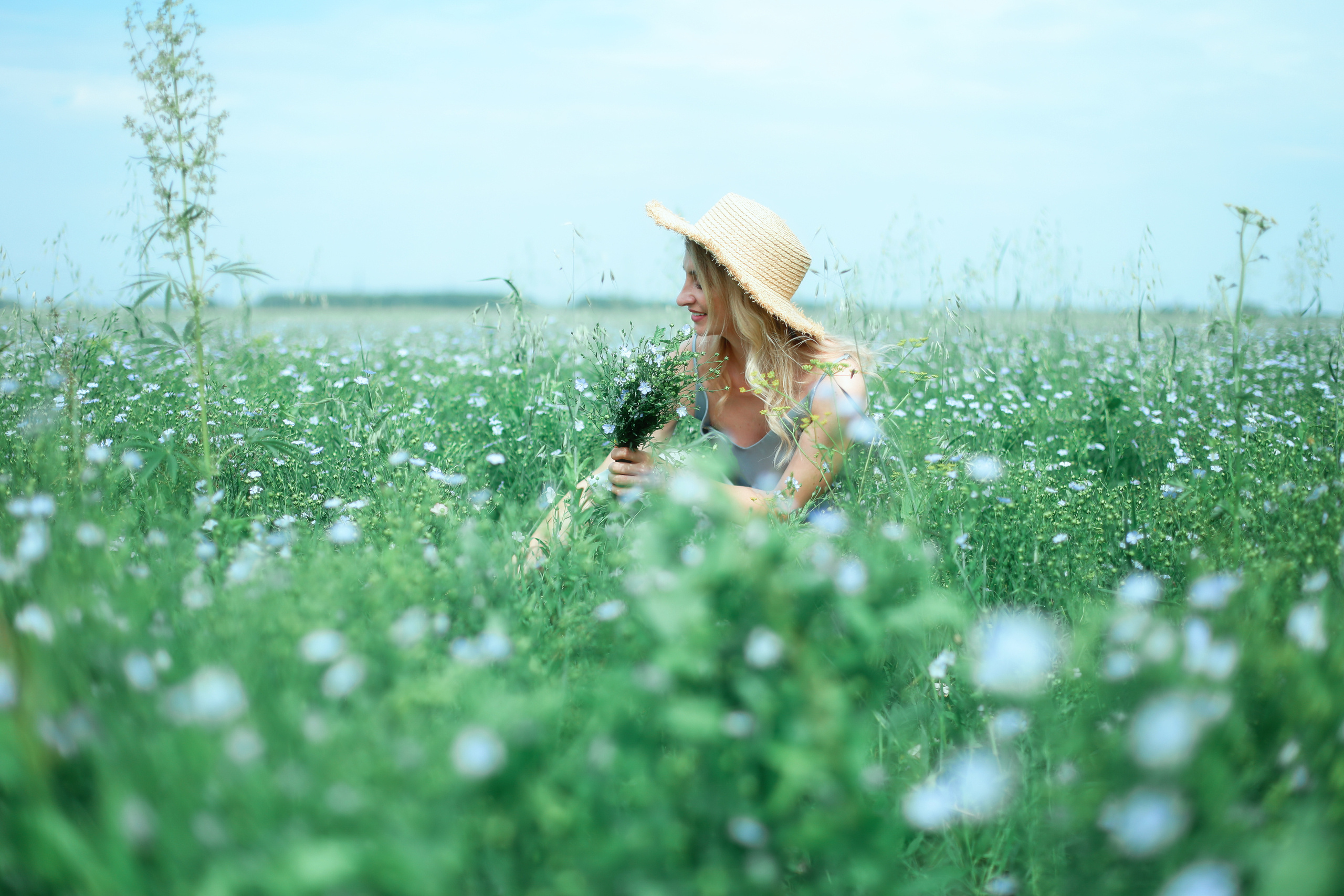 Девчонка сидит в цветочном поле с голубыми цветами и собирает букетик.